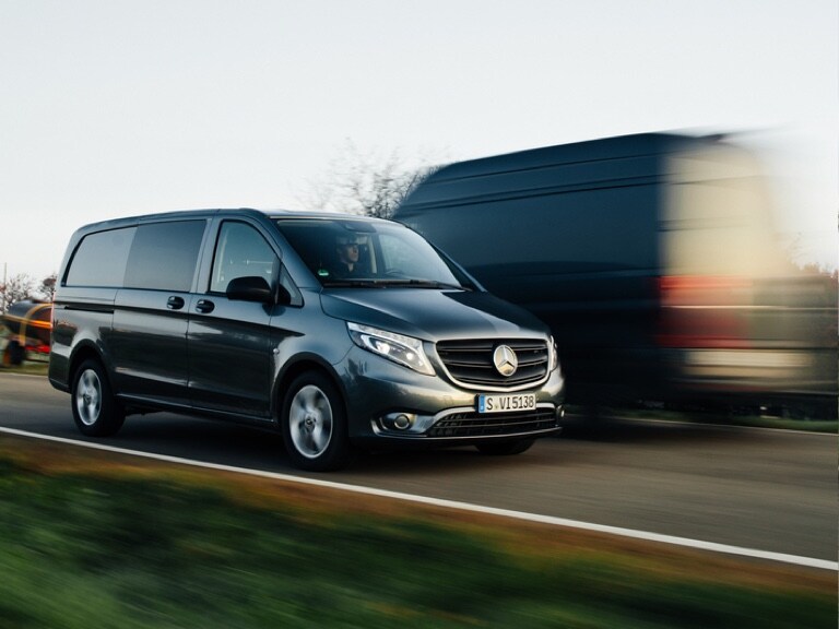 Zu sehen sind zwei verschiedene Mercedes-Benz Transporter, die auf einer Landstraße aneinander vorbeifahren.