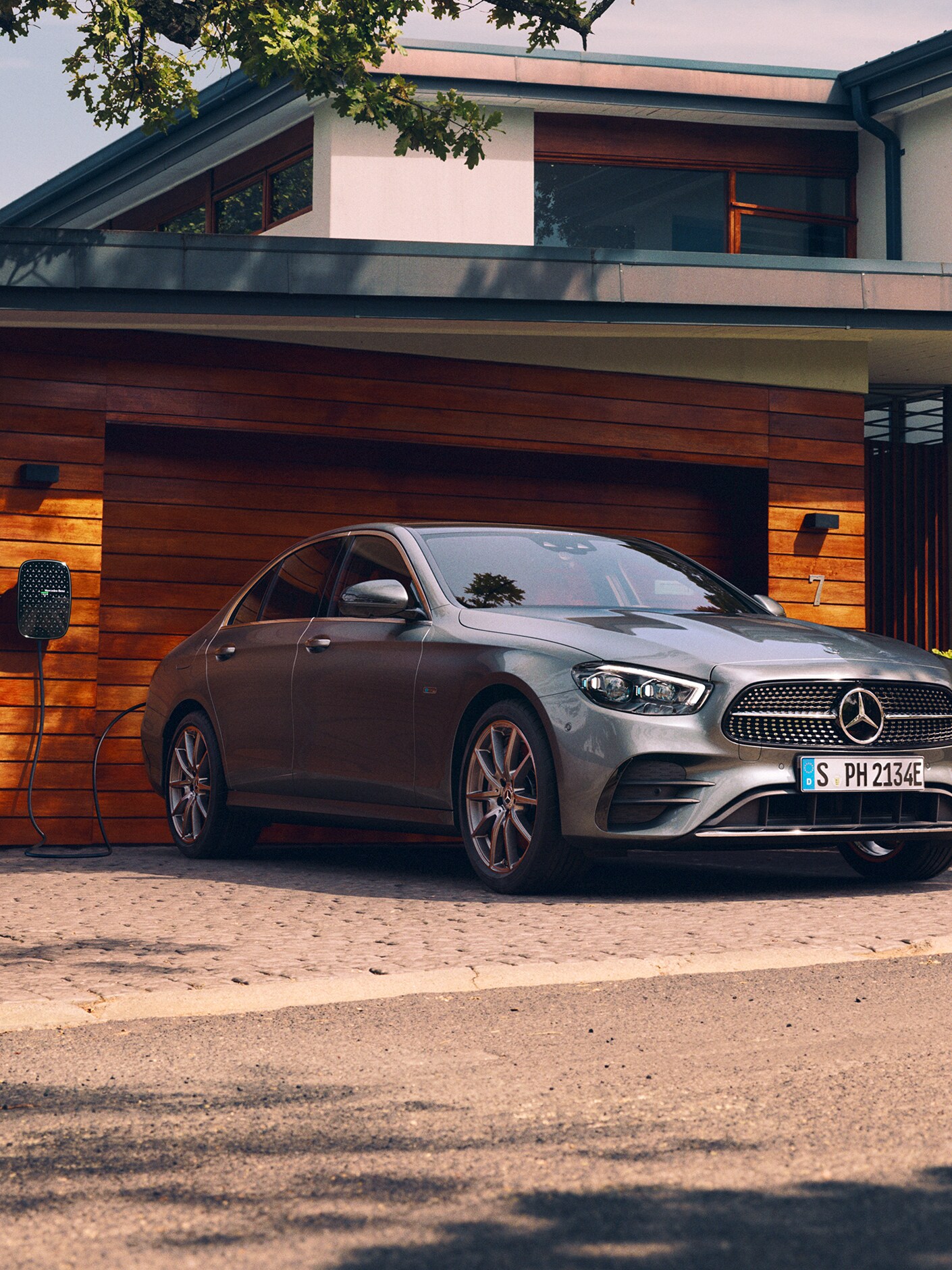 La photo montre la Mercedes-Benz Classe E Berline en cours de recharge devant un garage.
