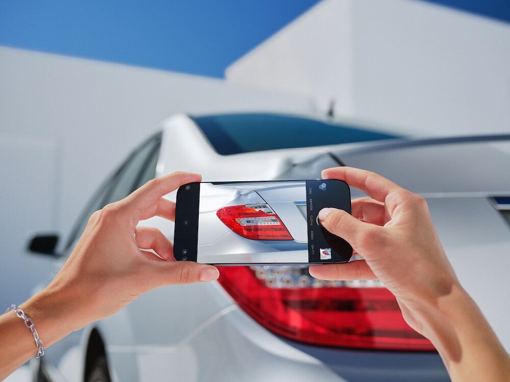 Jemand fotografiert einen Fahrzeugschaden an einem Mercedes-Benz mit dem Smartphone.