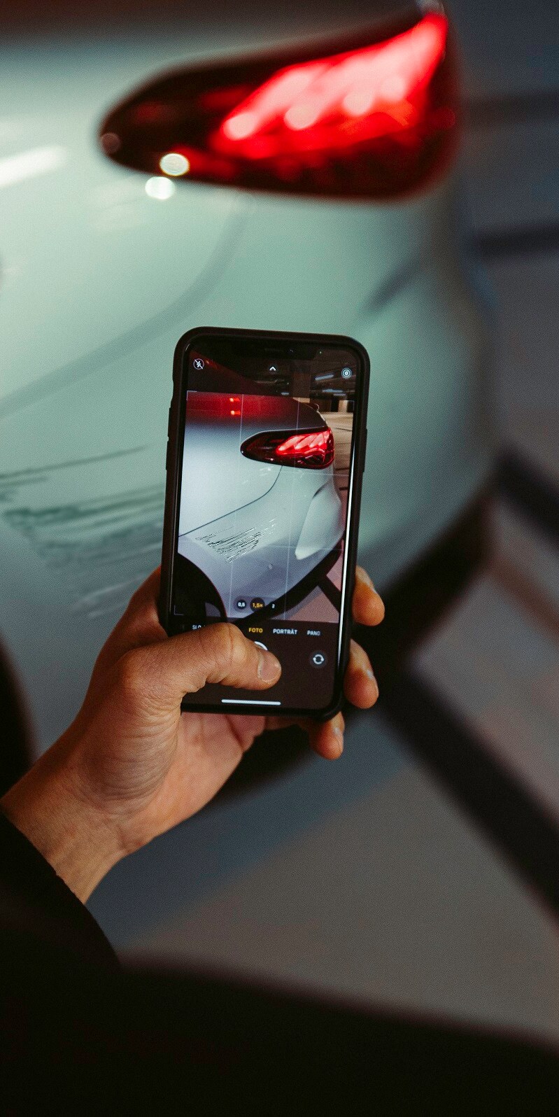 Avec un smartphone, un homme photographie les dégâts sur l'aile arrière de sa Mercedes.