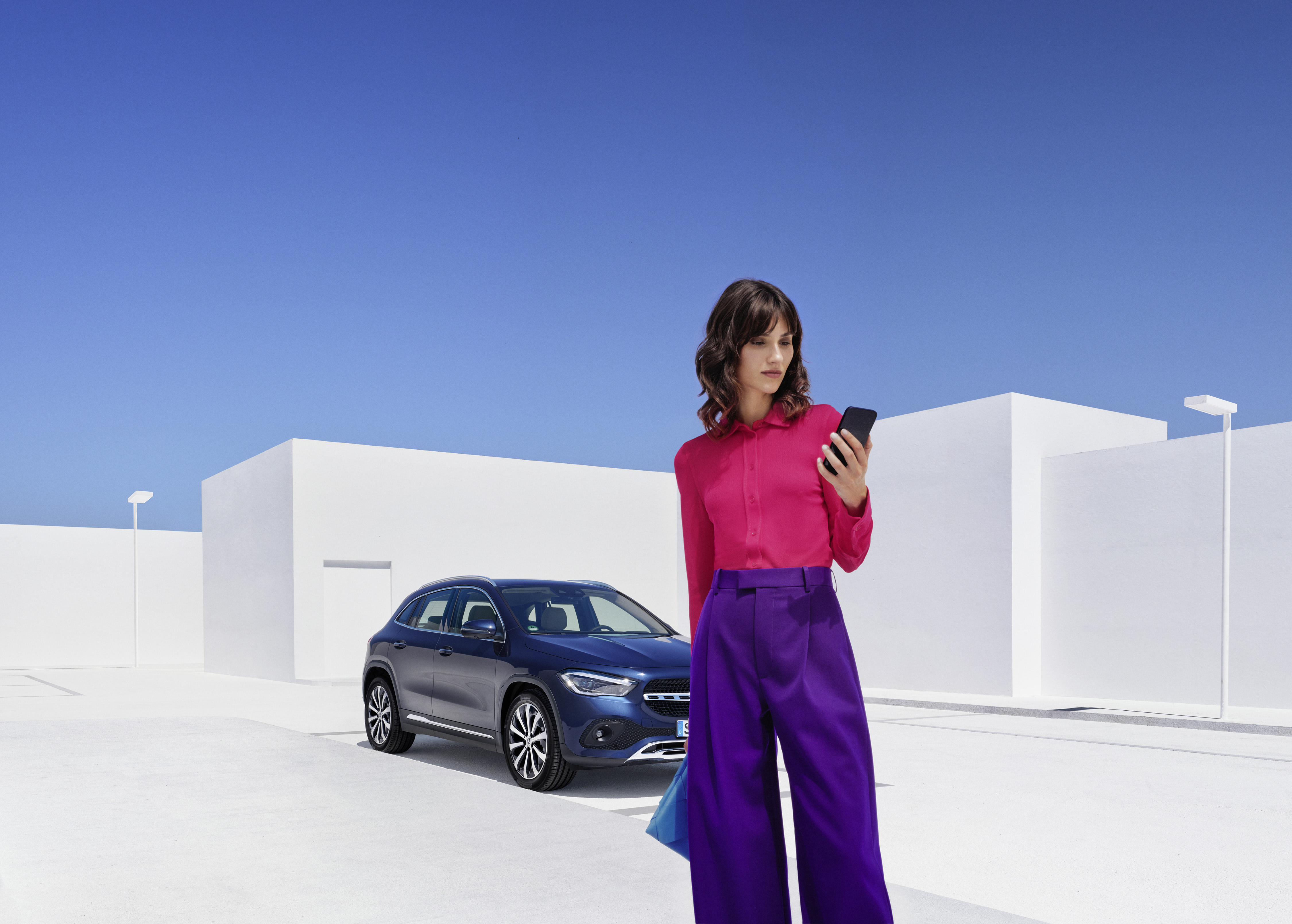 Centre d'assistance dépannage | Mercedes-Benz Une femme se tient devant sa Mercedes-Benz et consulte son smartphone.