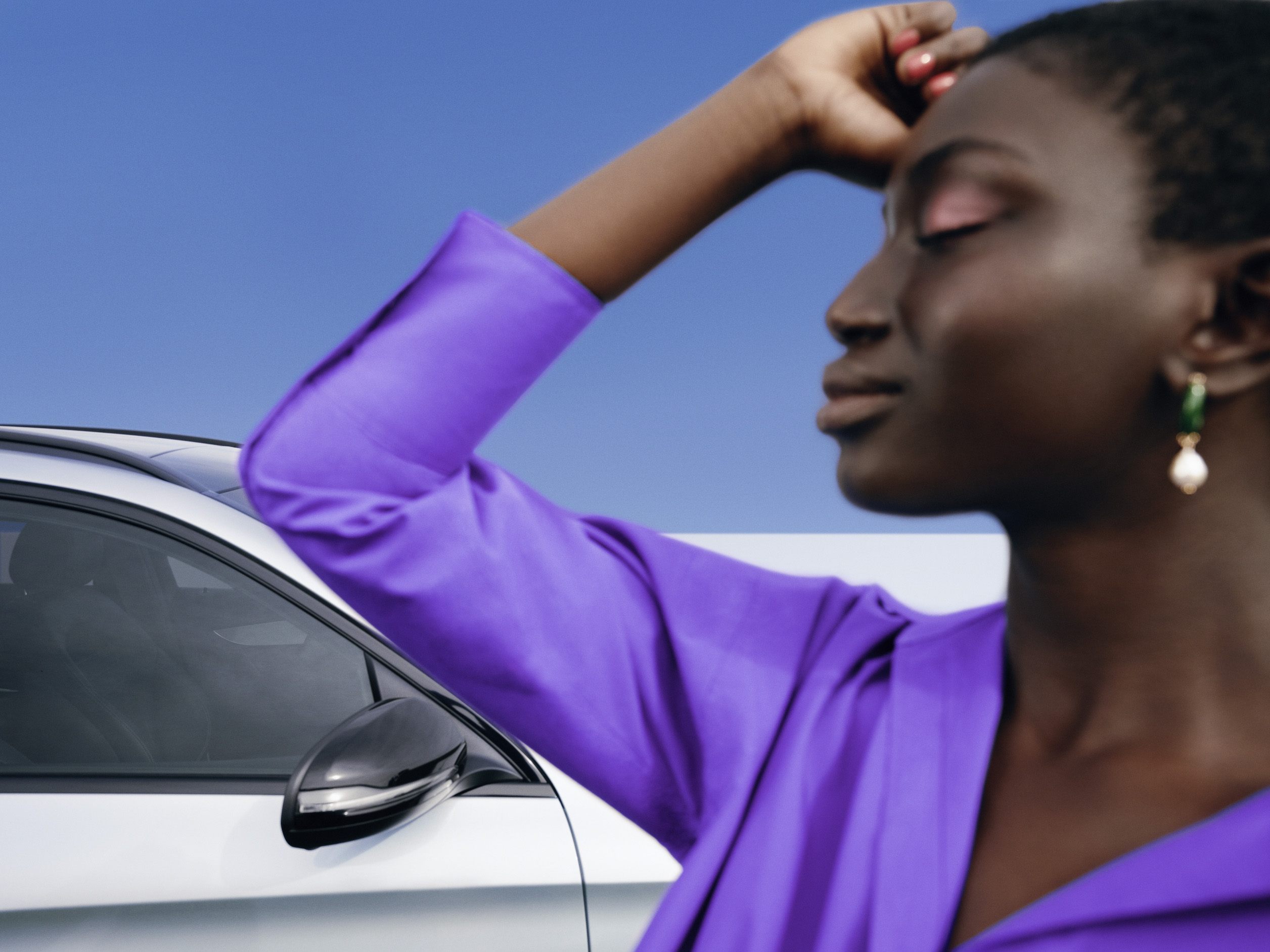 Mercedes-Benz | Original-Pflegeprodukte Eine Frau steht entspannt mit geschlossenem Gesichtsausdruck vor ihrem Mercedes.