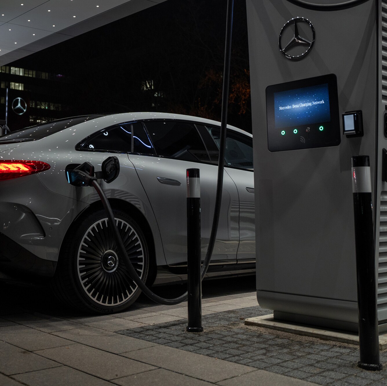 Das Bild zeigt eine nächtliche Szene, in der eine Mercedes-Benz EQS Limousine über ein Ladekabel mit einer Hochleistungsladestation verbunden ist.