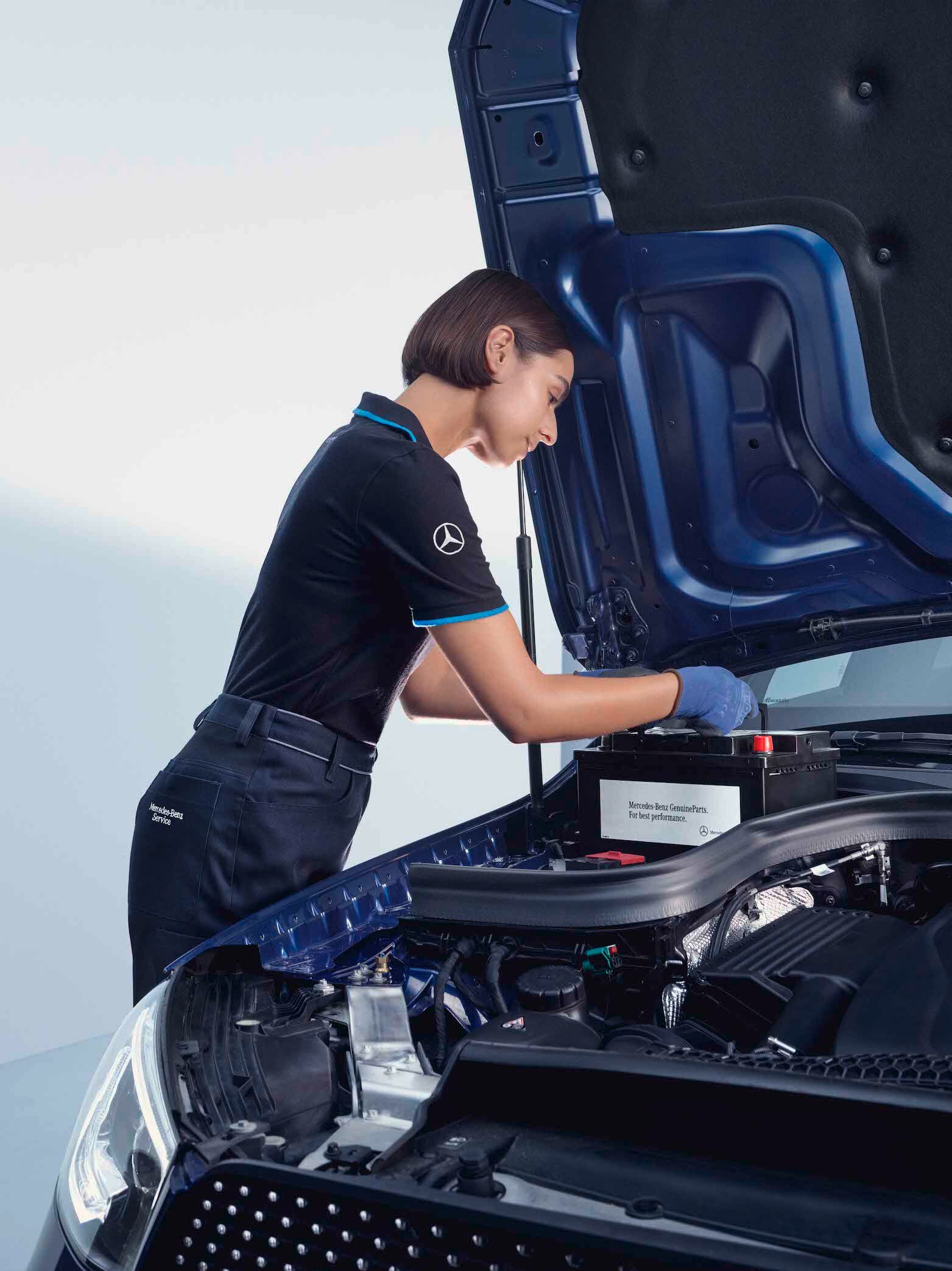 Eine KFZ-Mechanikerin beugt sich über die geöffnete Motorhaube eines Mercedes-Benz.