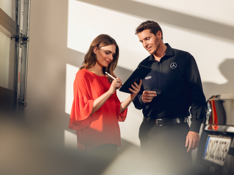 Schaden online melden Eine Kundin füllt, zusammen mit einem Mercedes-Benz Techniker, ein Formular auf einem Tablet aus.