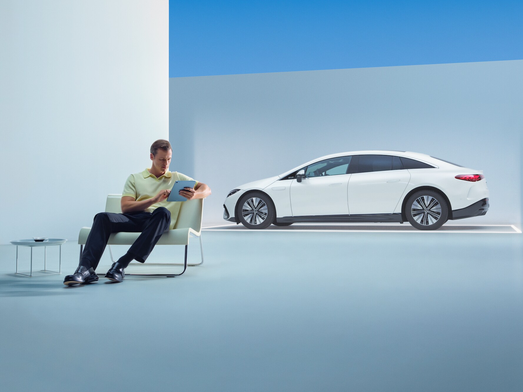 Un homme détendu est assis devant sa Mercedes avec sa tablette.