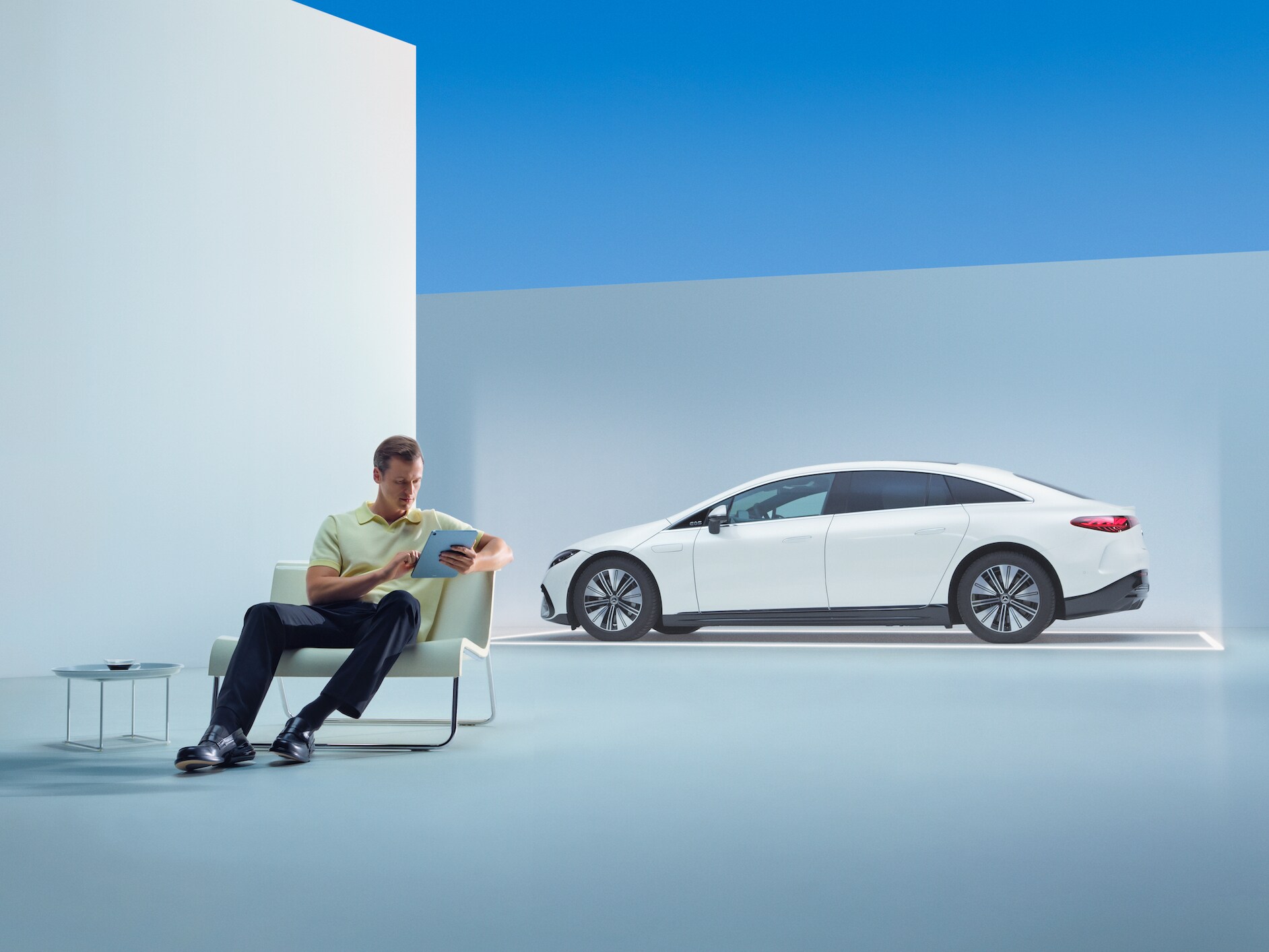 Eine entspannter Mann sitzt mit seinem Tablet vor seinem Mercedes.
