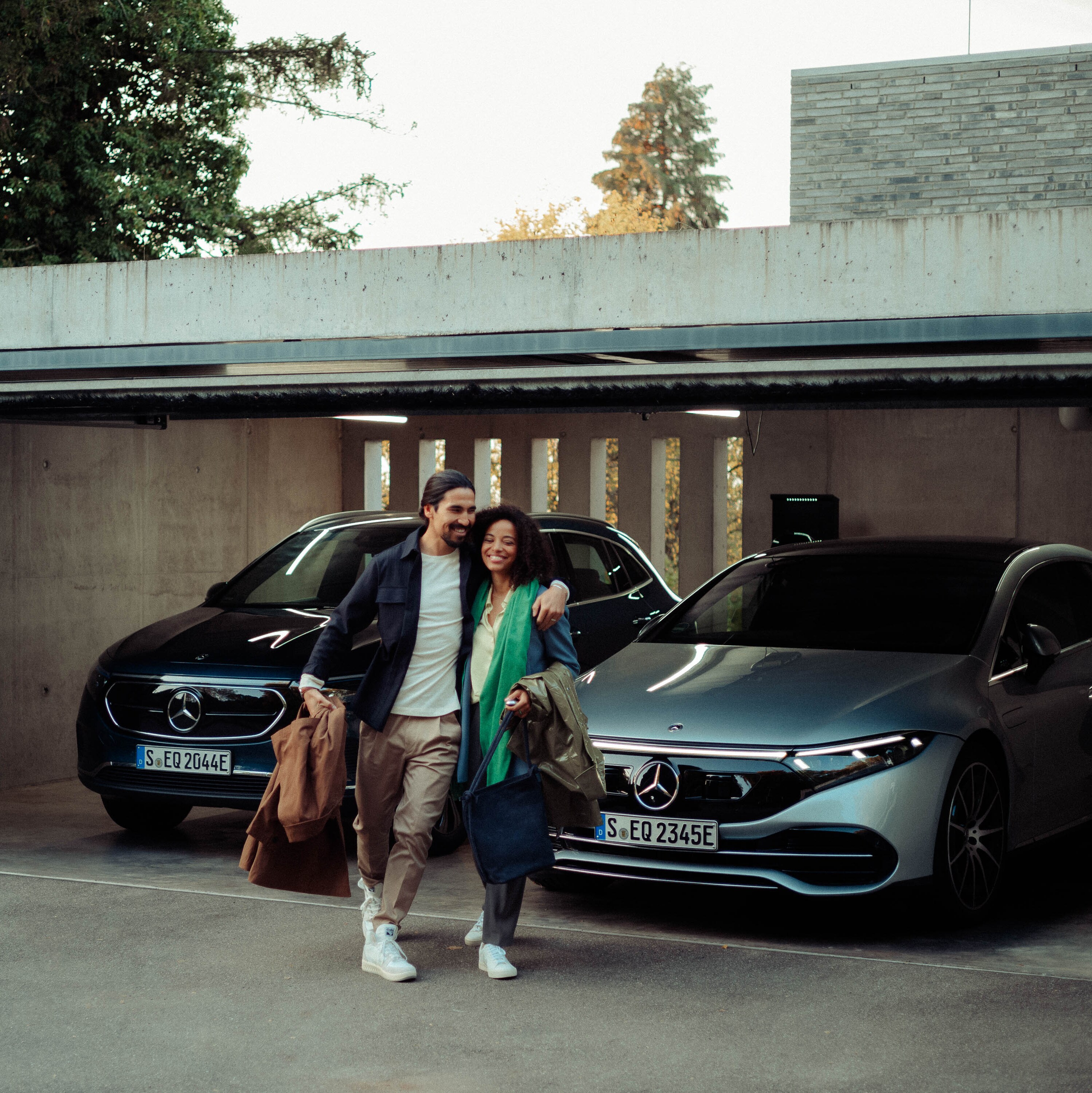 Une femme et un homme quittent un garage dans lequel sont garés une berline EQS et un EQA.