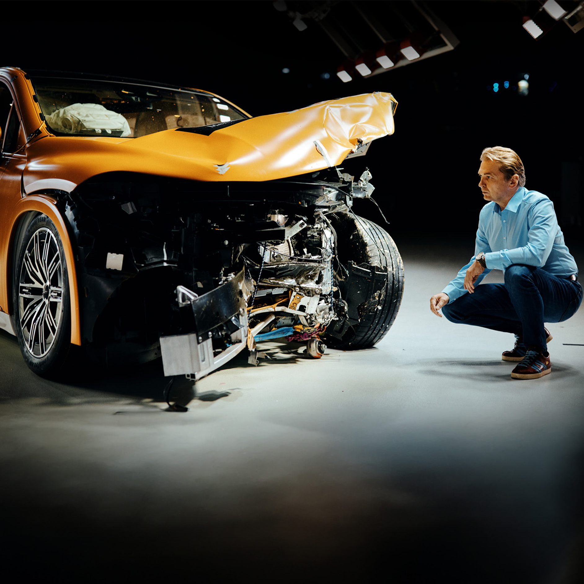 Expert en essais de collision | Sécurité | Mercedes-Benz Un expert en essais de collision examine une voiture Mercedes-Benz accidentée à l'avant en s'accroupissant à côté d'elle.