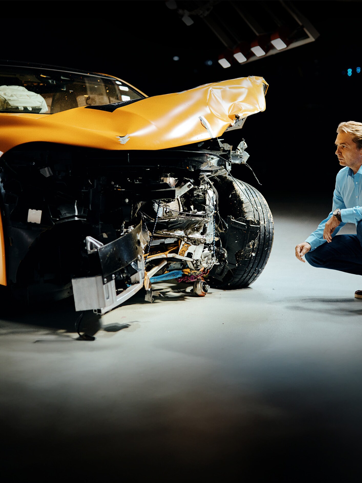 Un expert en crash-tests examinant un véhicule Mercedes-Benz accidenté à l'avant, accroupi à côté.