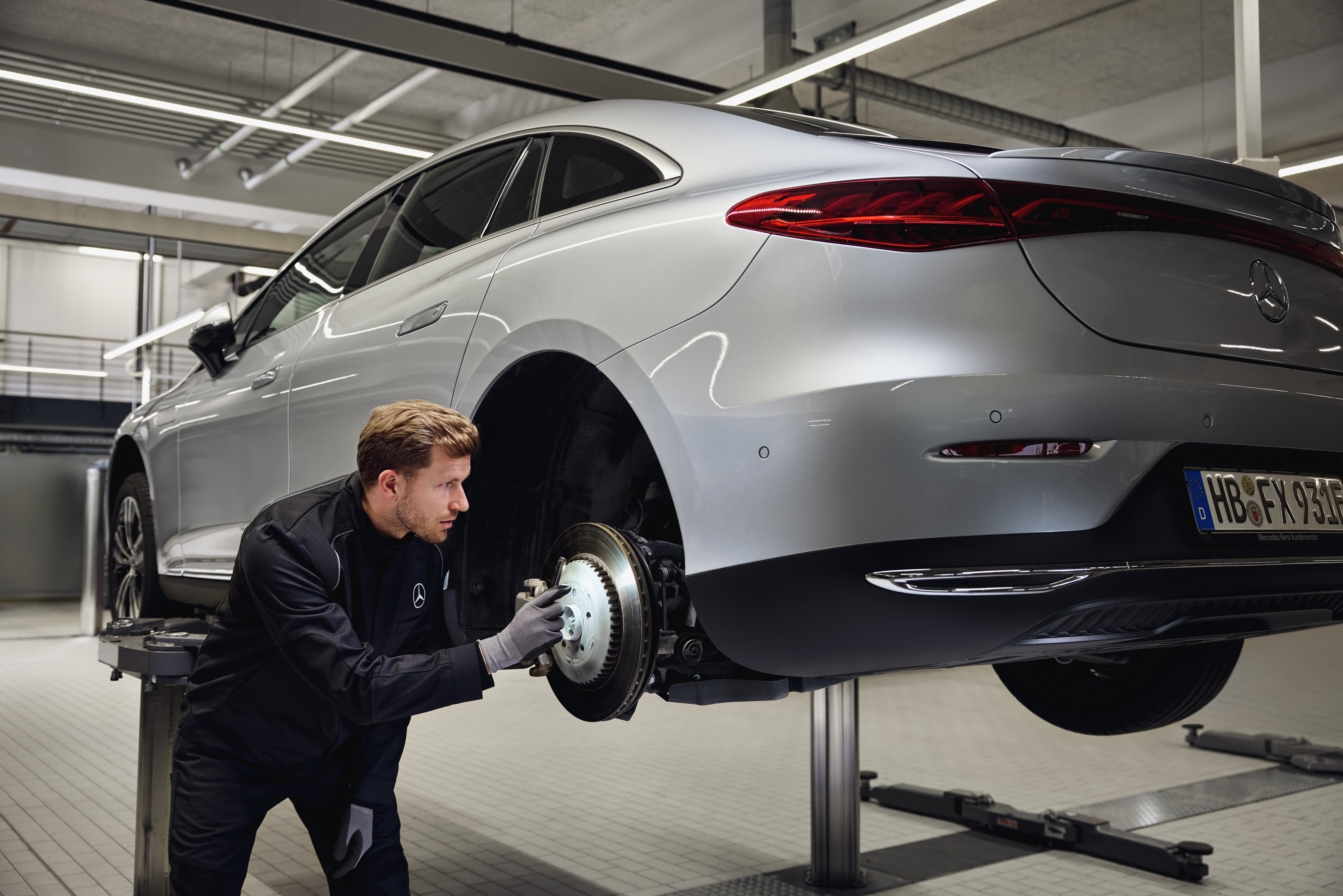 Remplacement des freins d'origine Mercedes-Benz Un véhicule Mercedes-Benz surélevé sur un pont élévateur, avec un technicien en train d'inspecter le système de freinage arrière dans le cadre d'une maintenance avec remplacement de pièces d'origine.
