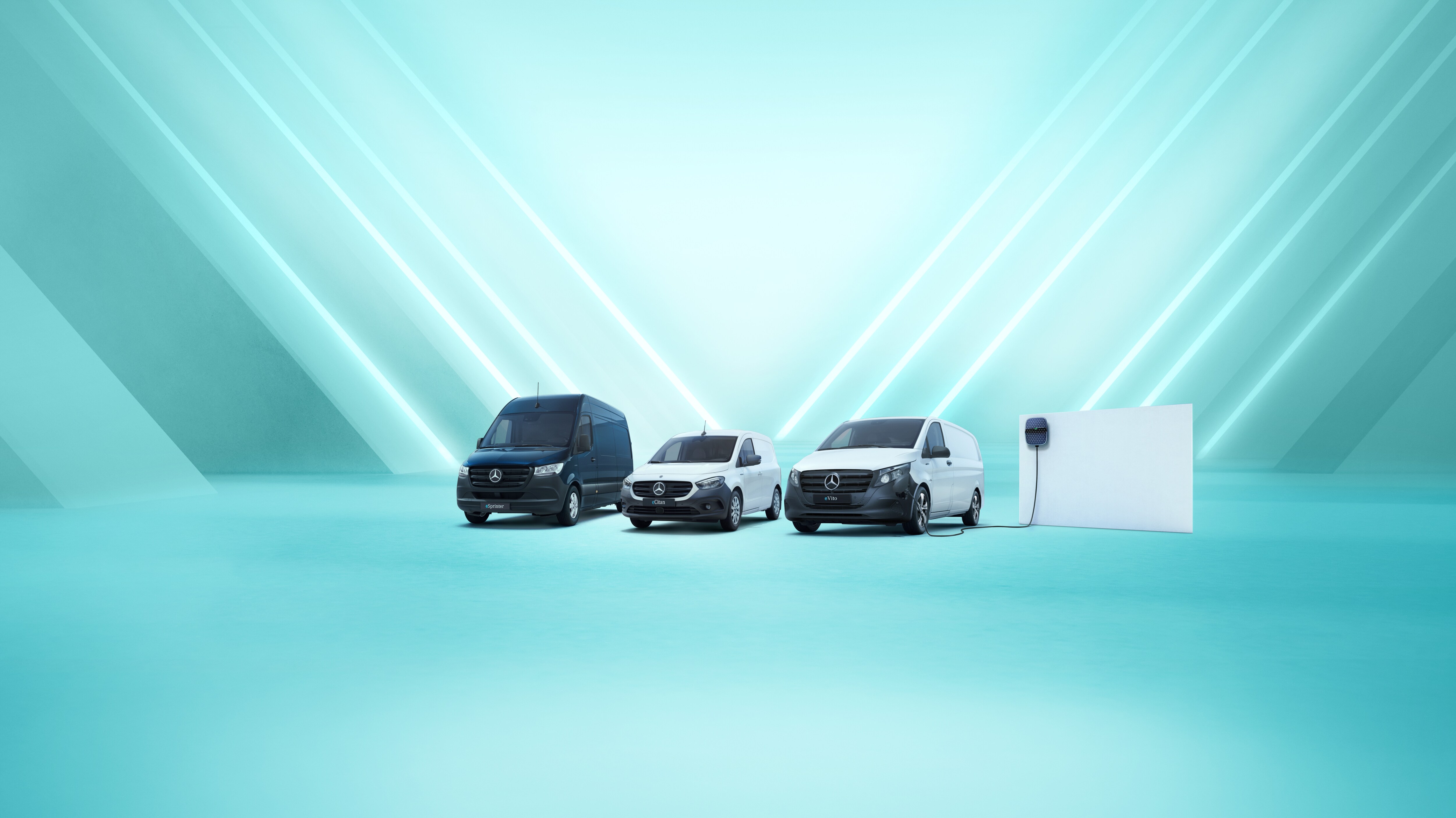 The Mercedes-Benz eSprinter, eCitan and eVito are lined up on display, with the eVito docked at a charging station. 