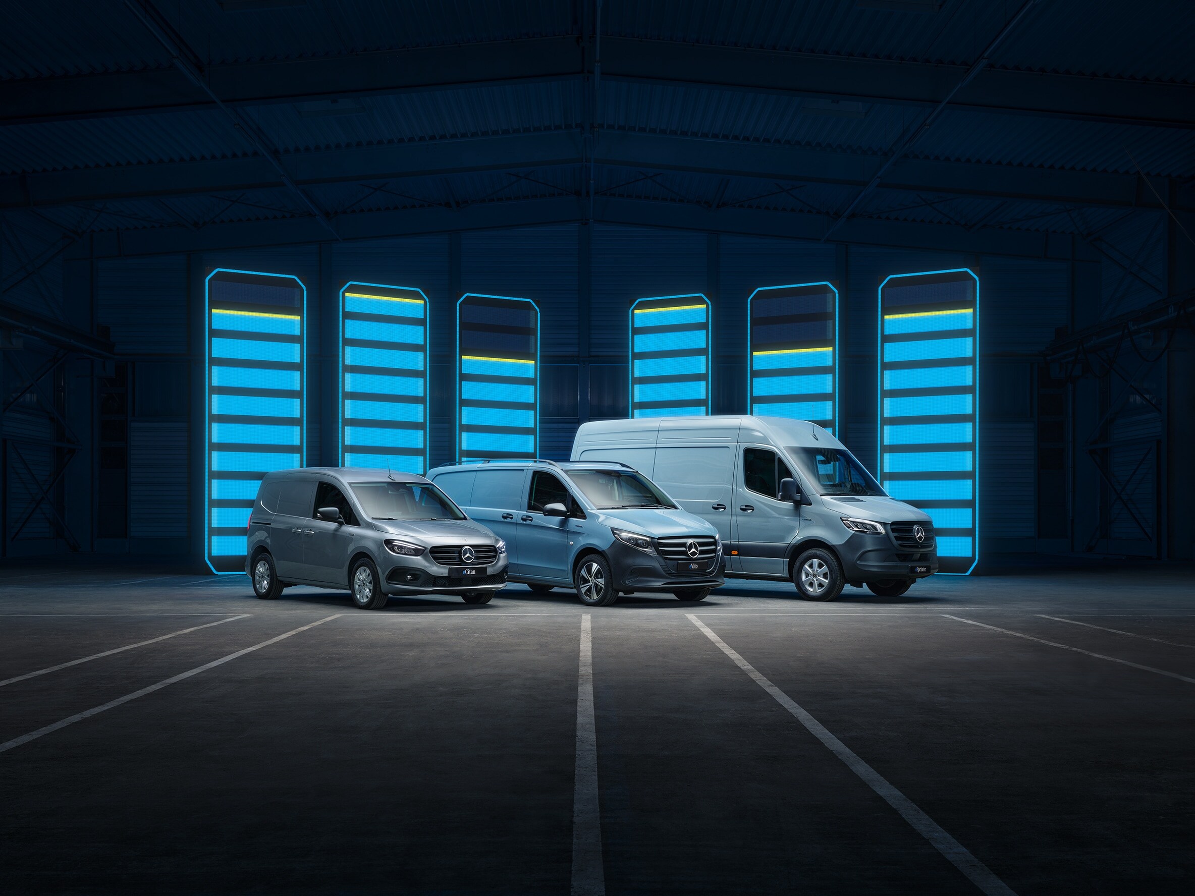 La gamme d'utilitaires légers électriques Mercedes-Benz exposée dans un entrepôt au design futuriste, avec des bornes de recharge lumineuses