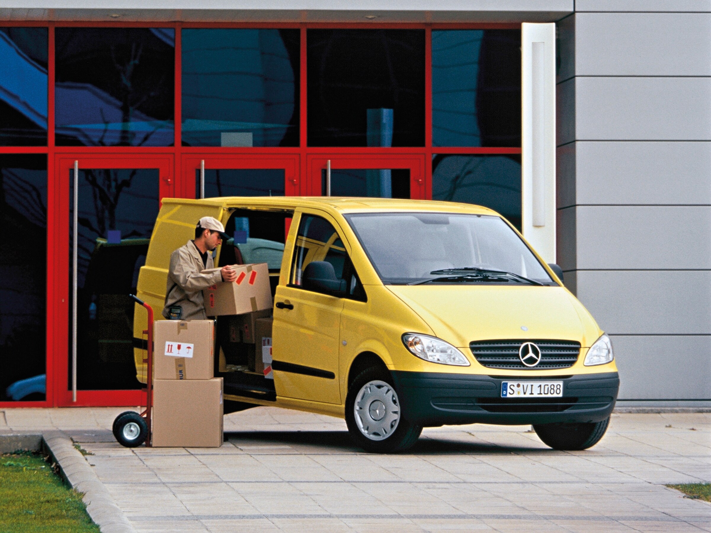 Un Mercedes-Benz Vito jaune garé devant un immeuble, avec un employé en train de décharger des colis