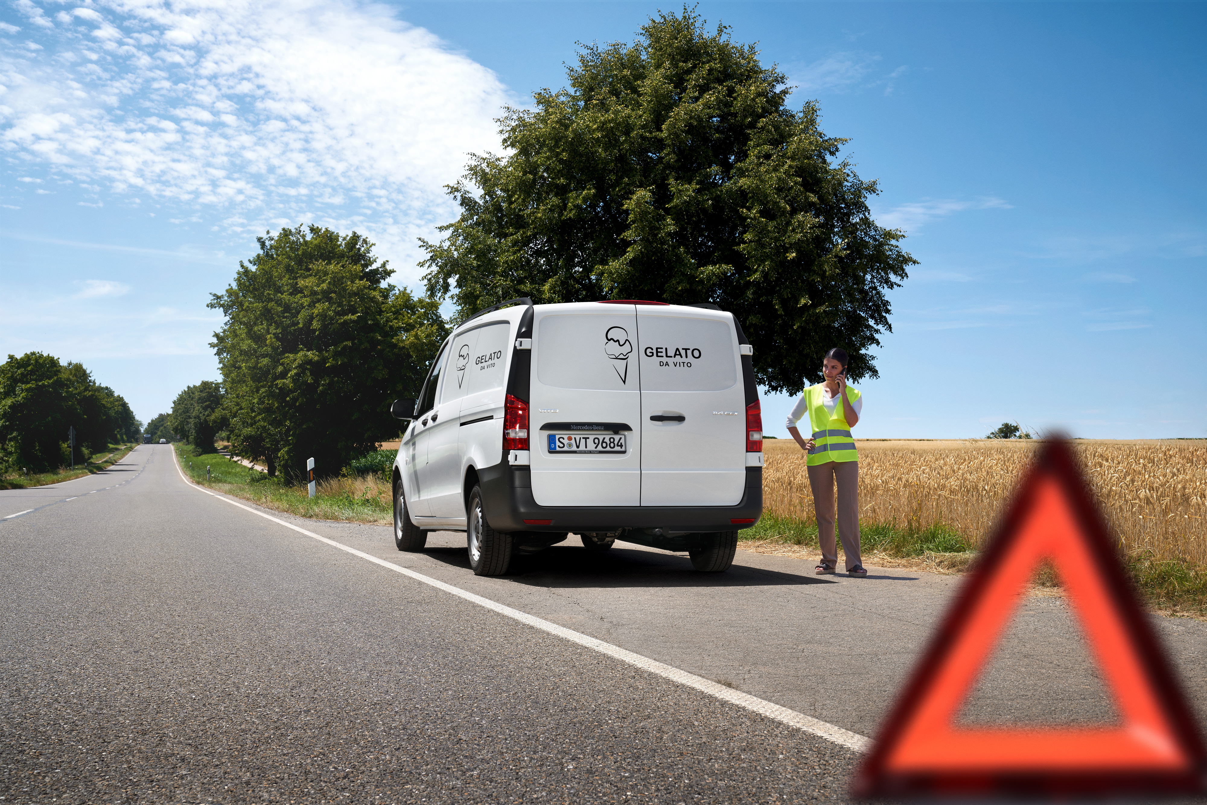 Mercedes-Benz | Assistance pour utilitaires légers | Service24h Une femme appelle la ligne d'assistance du Mercedes-Benz Service 24h, disponible 24 heures sur 24 ; un Mercedes-Benz Sprinter est garé sur le bord d'une route de campagne.