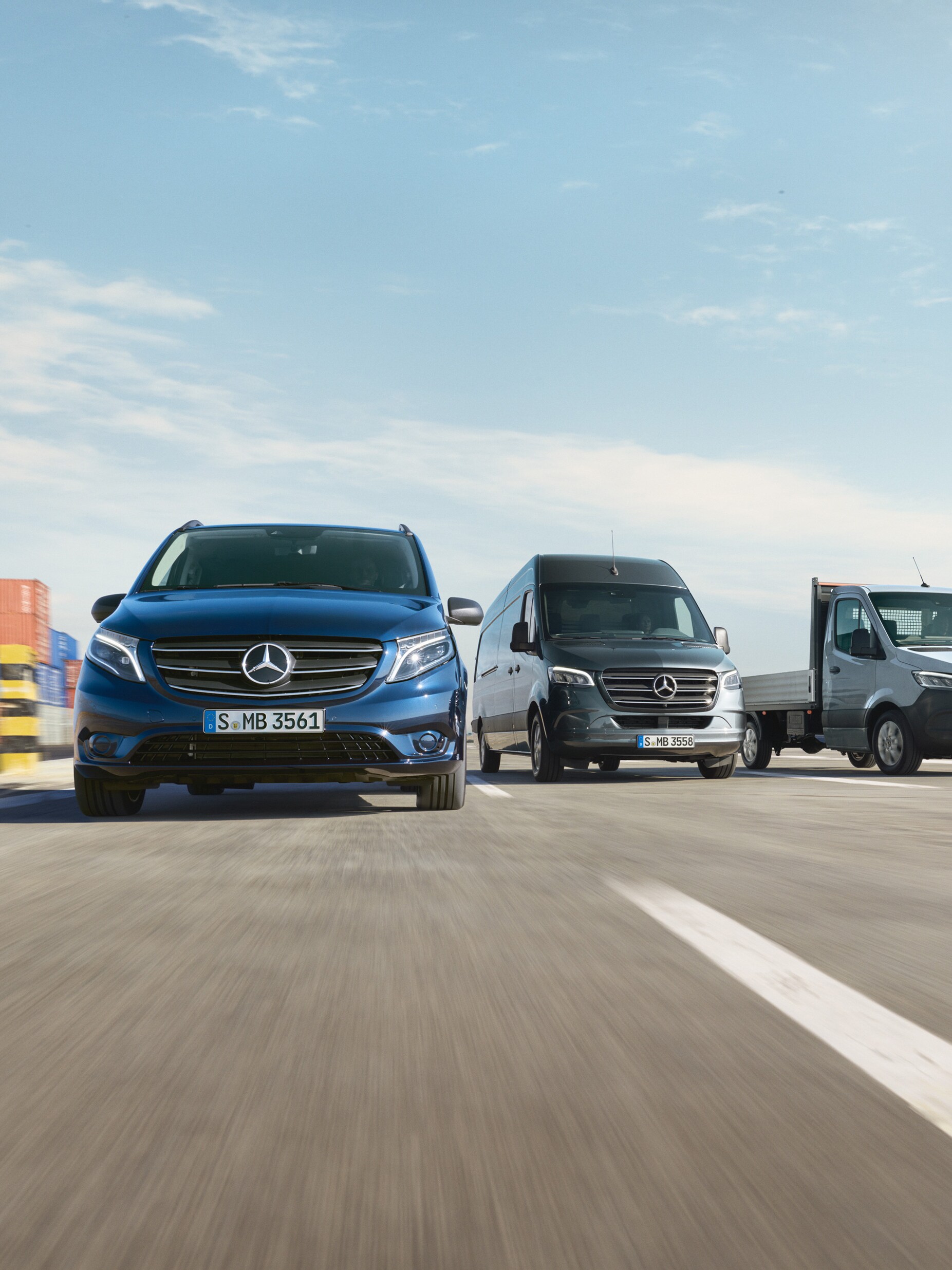 Eine Reihe von Mercedes-Benz Transportern, die nebeneinander auf einer Straße neben einer Laderampe geparkt sind.