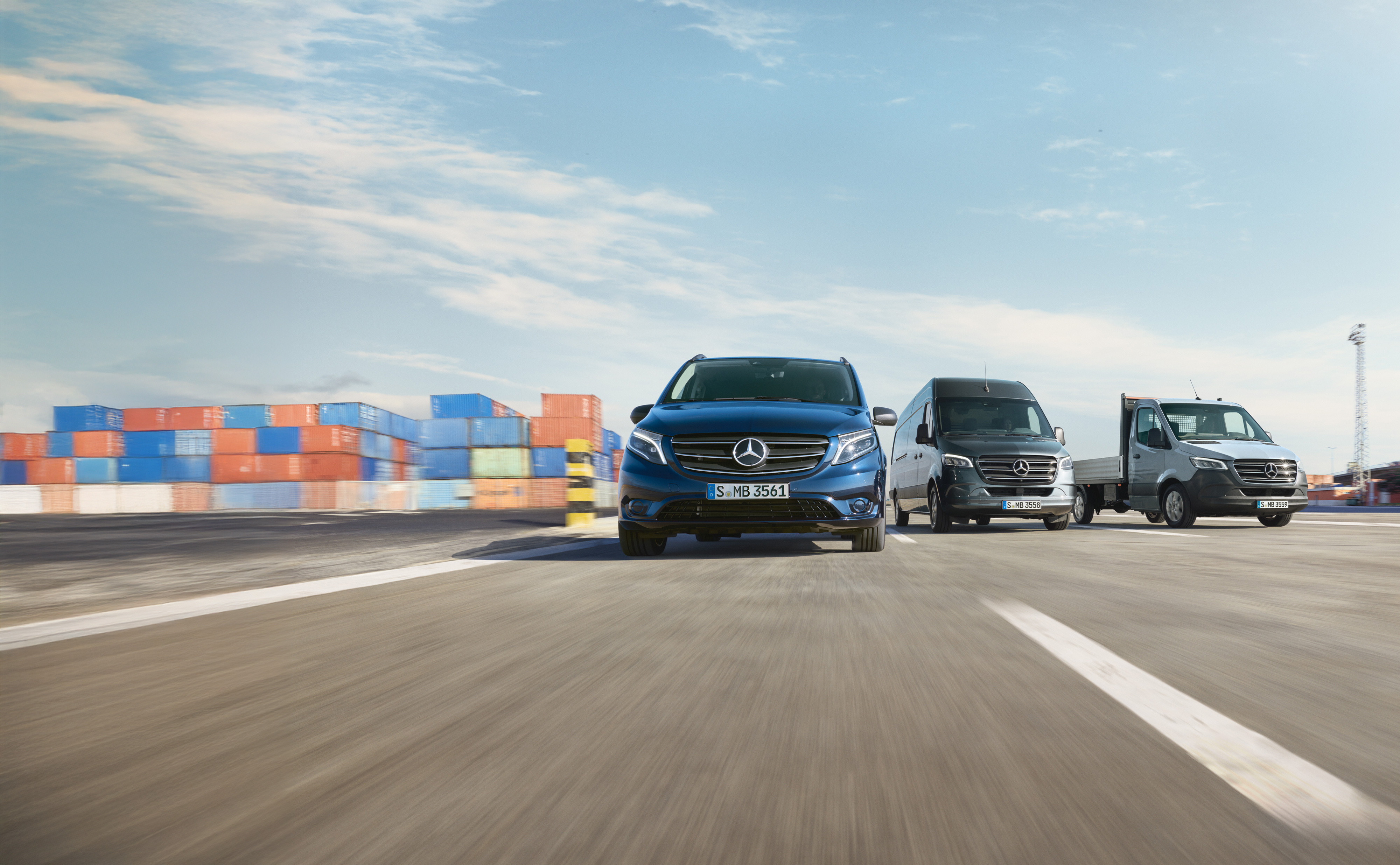 Mercedes-Benz | Transporterbetreuung | Service24h Eine Reihe von Mercedes-Benz Transportern, die nebeneinander auf einer Straße neben einer Laderampe geparkt sind.