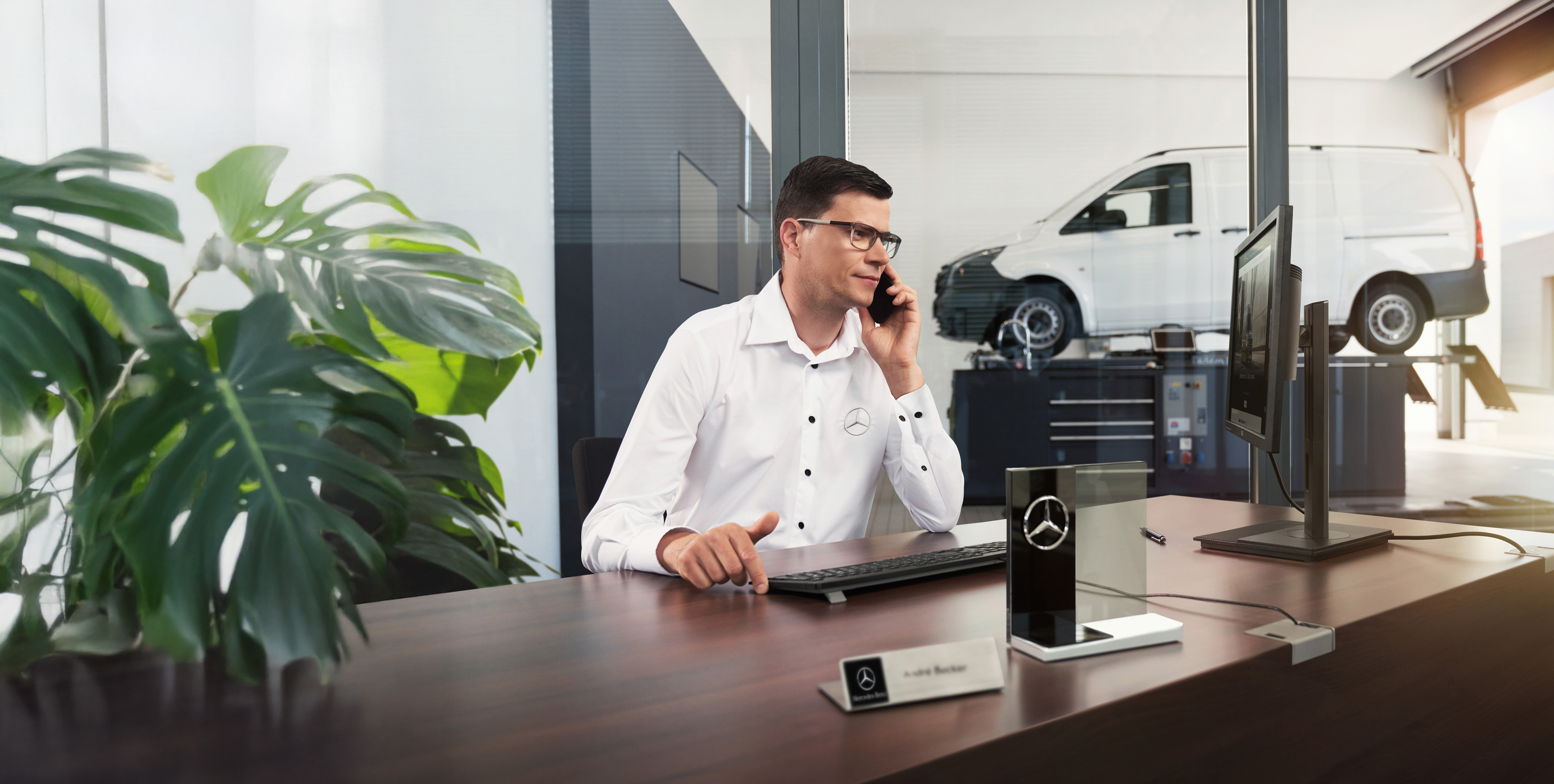 Mercedes-Benz | Transporterbetreuung Mercedes-Benz Mitarbeiter telefoniert an einem Schreibtisch mit einem Mercedes-Benz Vito Transporter in der Werkstatt.
