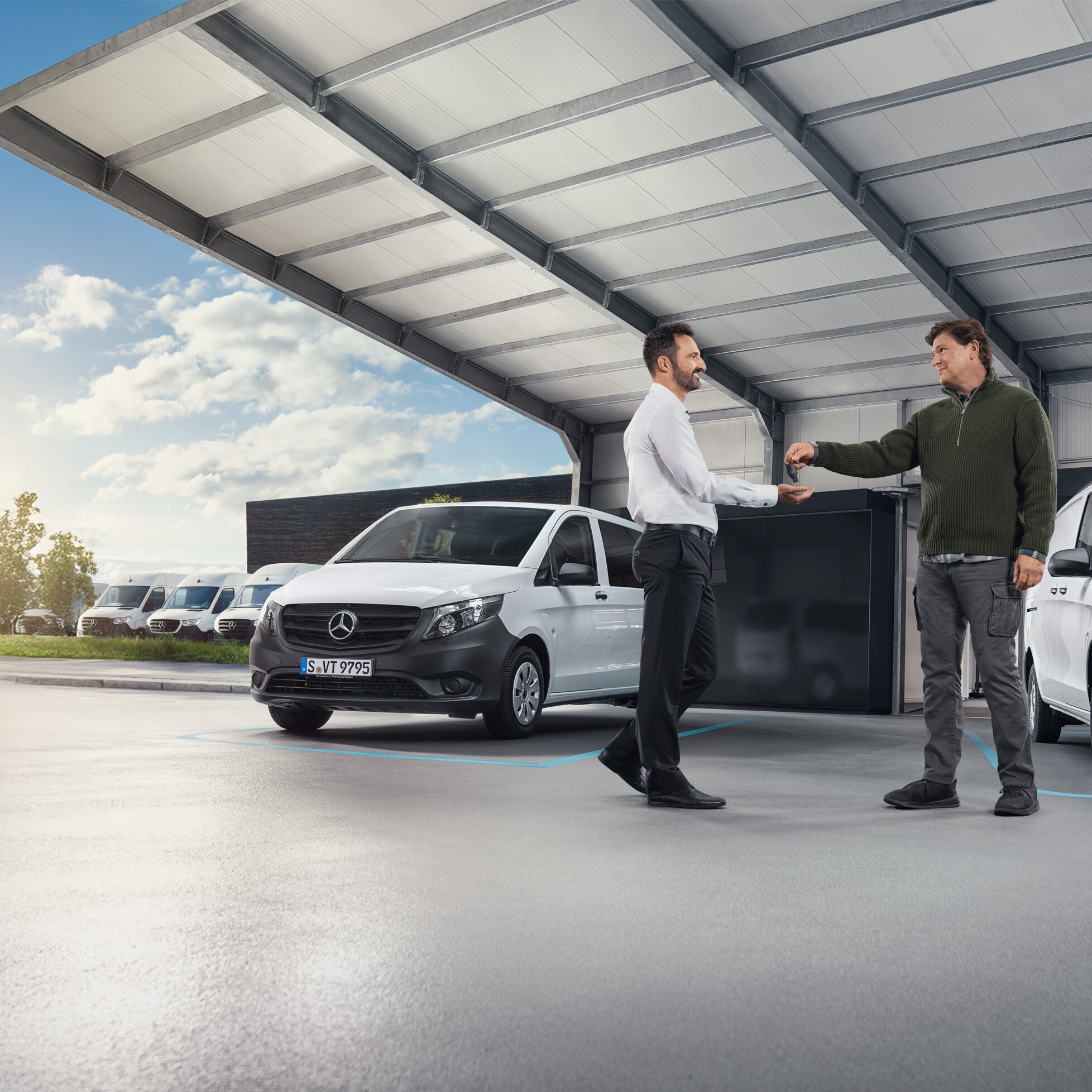 Zwei Männer im Gespräch vor einer Reihe weißer Mercedes-Benz Nutzfahrzeuge in einer Halle.