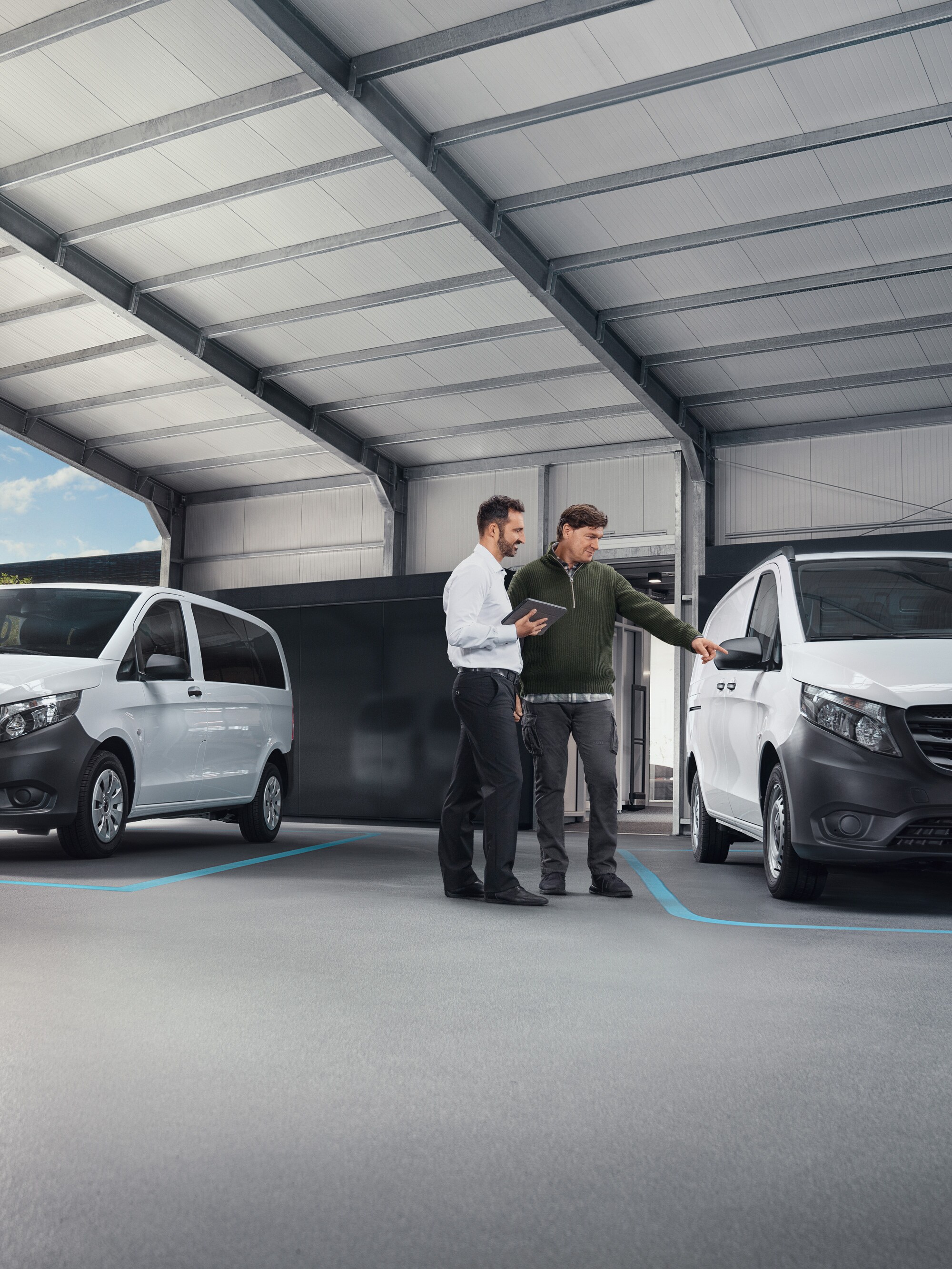 Zwei Personen unterhalten sich in einer Werkstatt vor zwei weißen Mercedes-Benz Transportern.