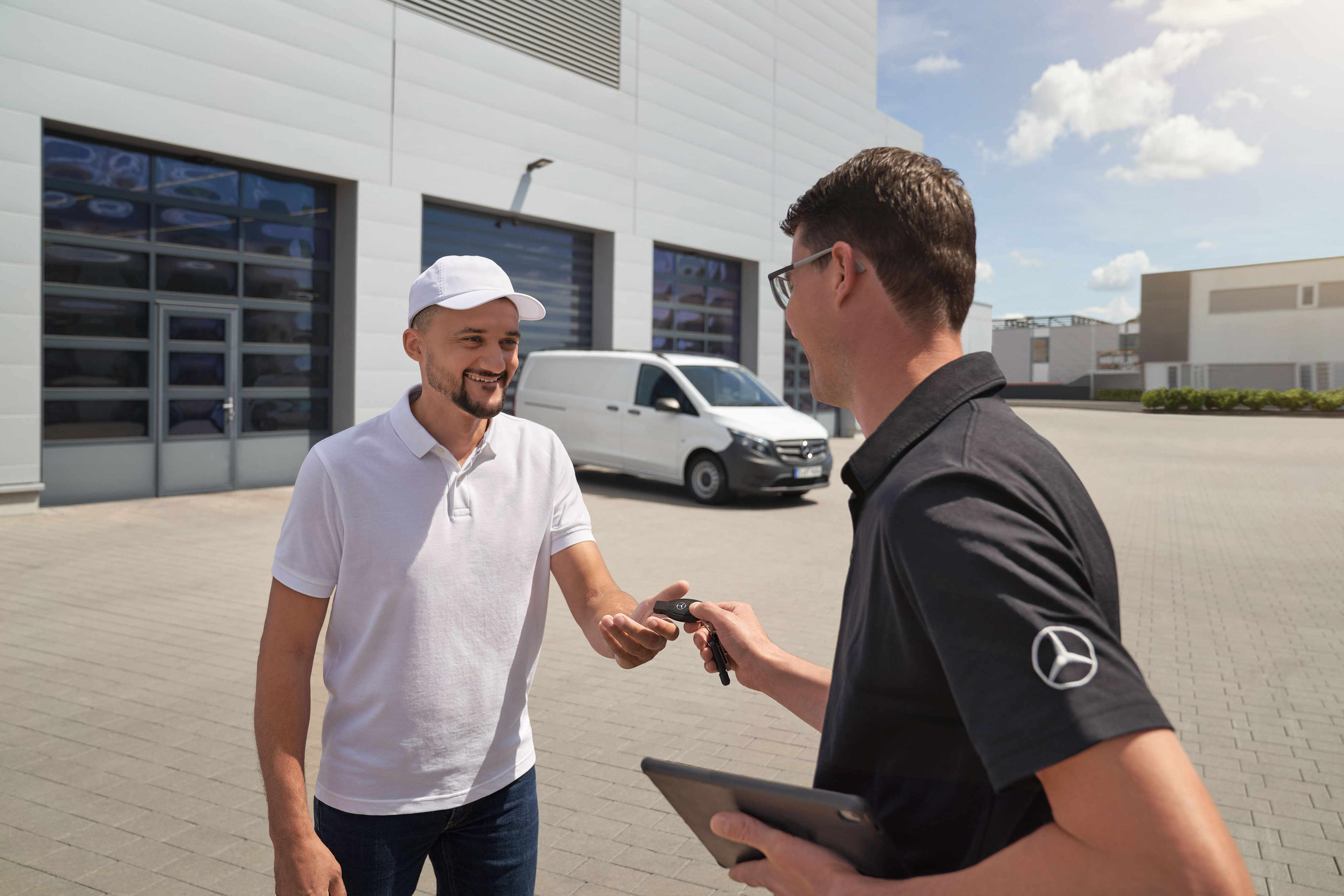 Mercedes-Benz | Komfort | Abhol- und Bringservice Mercedes-Benz Techniker bei der Schlüsselübergabe an einen Kunden mit einem weißen Mercedes-Benz Vito Transporter im Hintergrund.