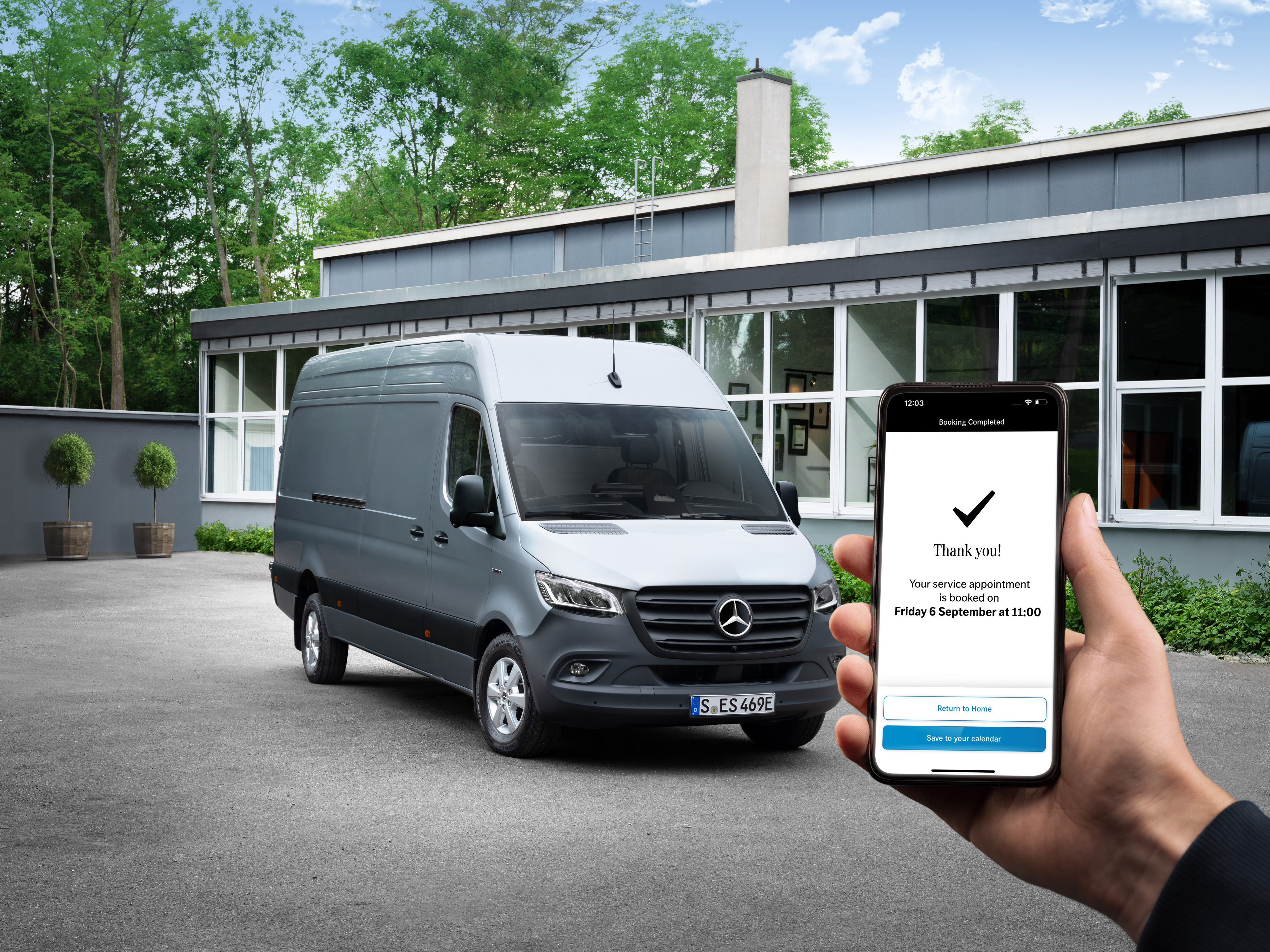 Mercedes-Benz | Komfort | Servicepartner Ein grauer Mercedes-Benz Sprinter Transporter vor einem Büro mit einer Person, die ein Smartphone in der Hand hält im Vordergrund.