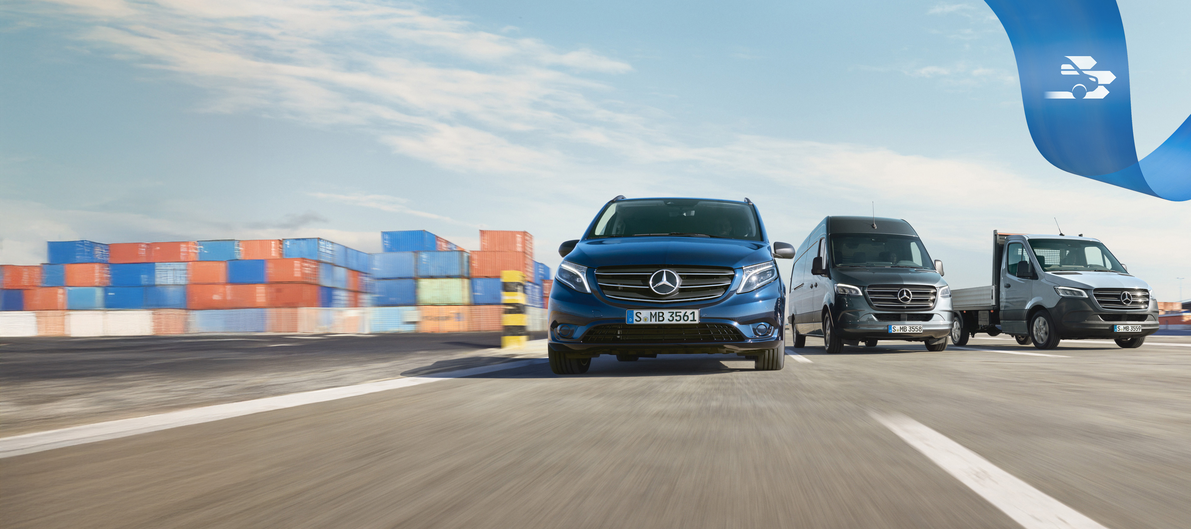 Mercedes-Benz | Komfort MobiloVan Eine Reihe von Mercedes-Benz Transportern auf der Straße mit Frachtcontainern im Hintergrund.