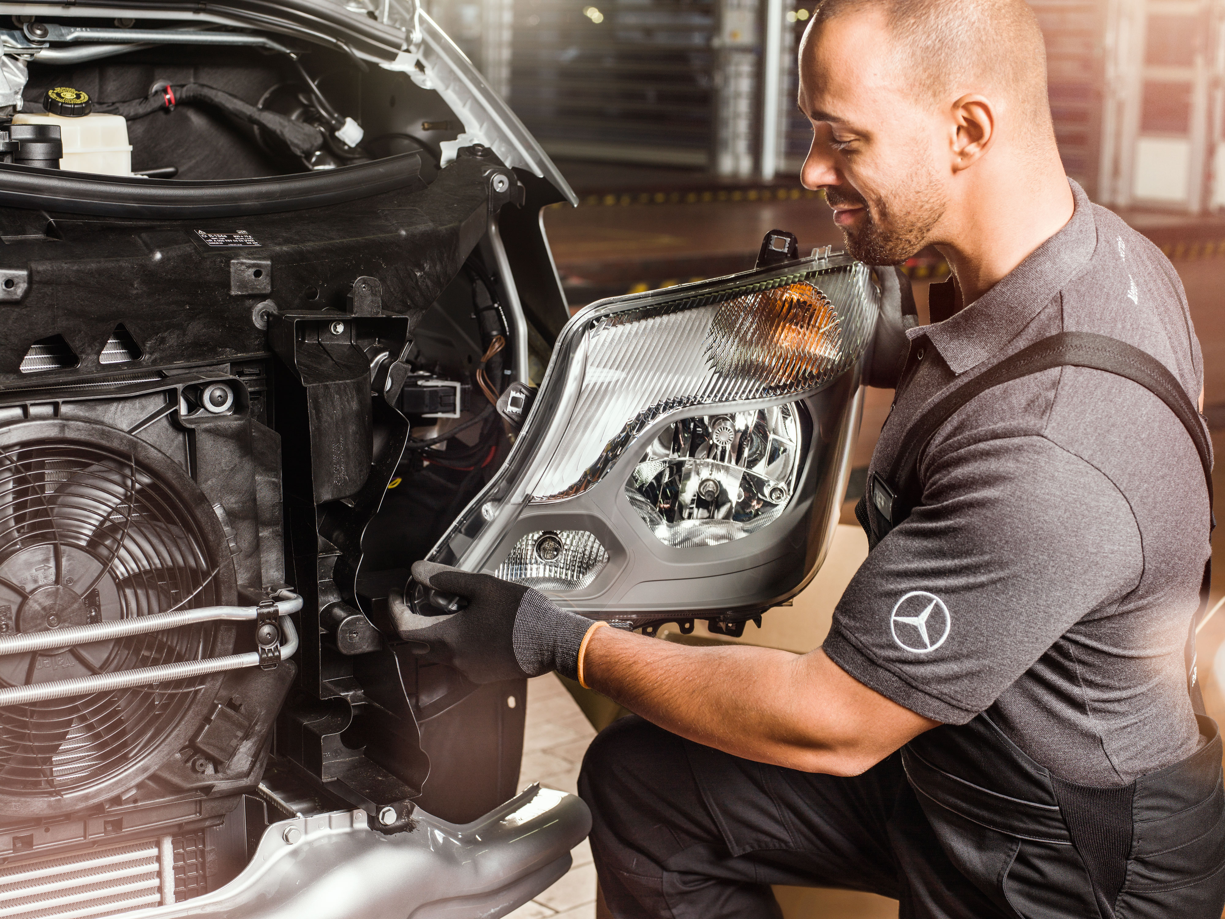 Mercedes-Benz | Pièces d'origine de qualité pour utilitaires légers Mécanicien vérifiant des pièces d'origine Mercedes-Benz devant le moteur ouvert d'un Sprinter, en consultant le catalogue de pièces de rechange Mercedes.