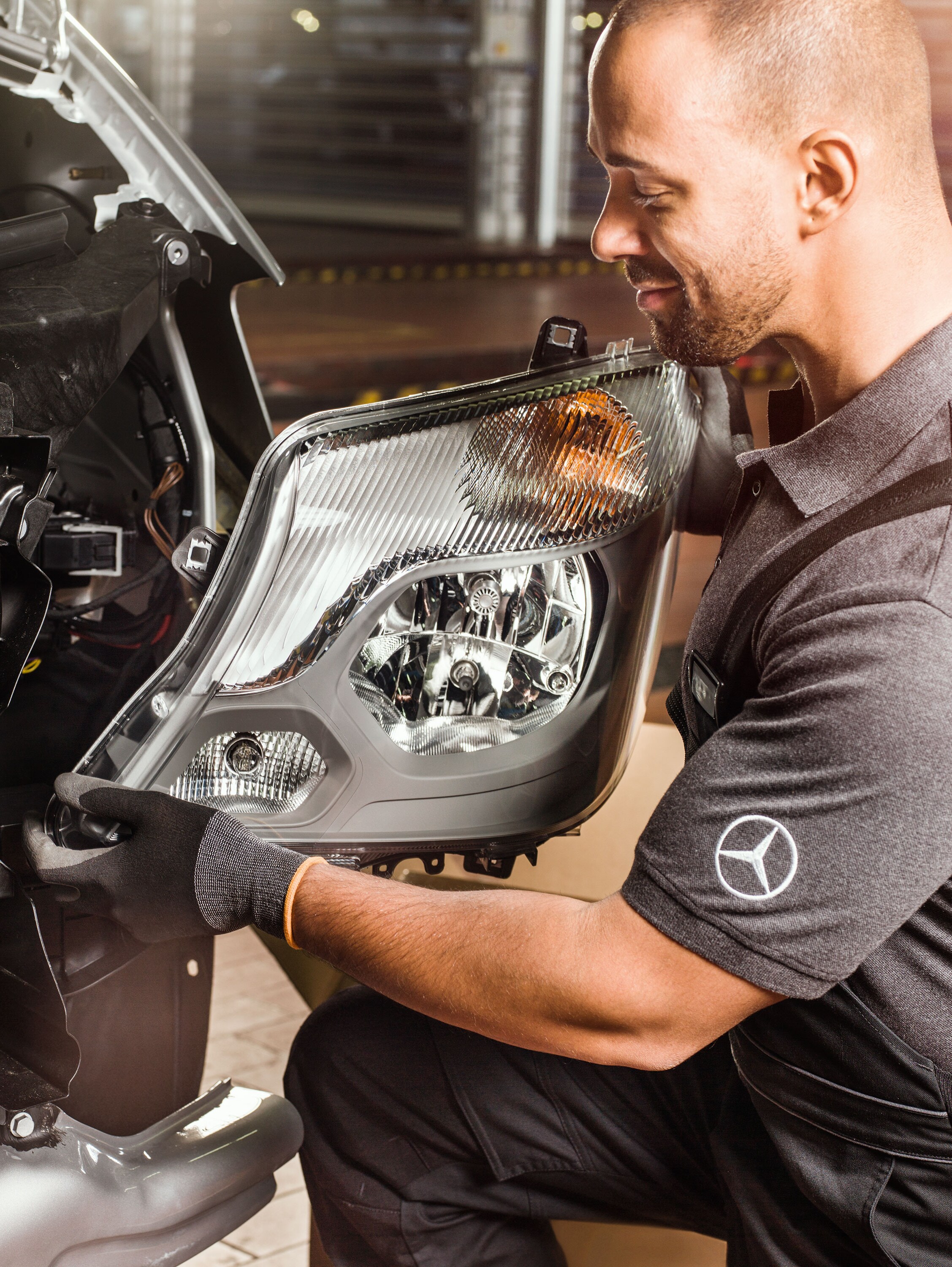 Mechaniker prüft Mercedes-Benz Original-Teile vor einem geöffneten Sprinter-Motor und gleicht sie mit dem Mercedes Ersatzteilkatalog ab.