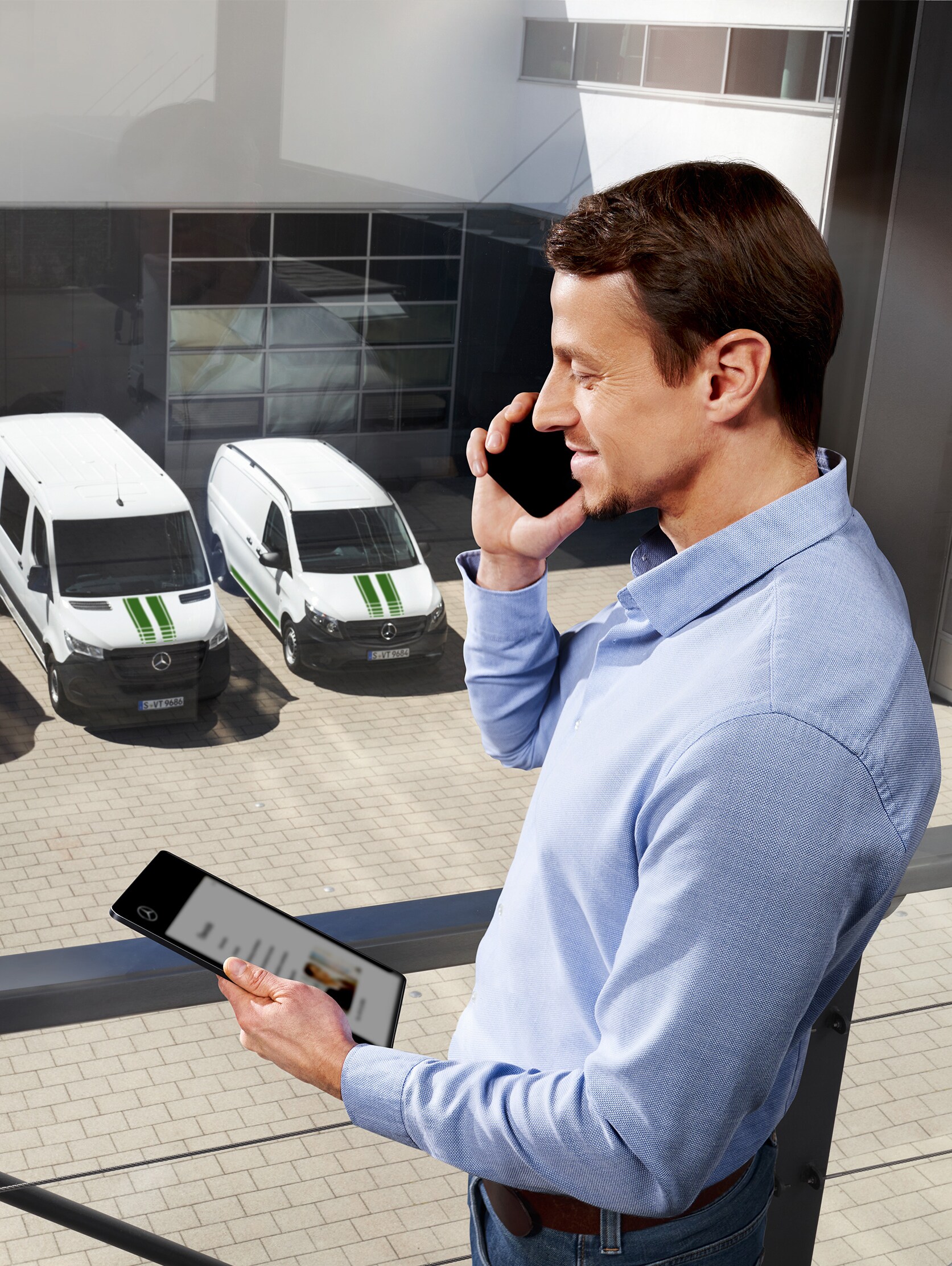 Mann am Telefon mit Tablet vor drei Mercedes-Benz Transportern, Thema: Wie lange ist die Herstellergarantie bei Mercedes-Benz?