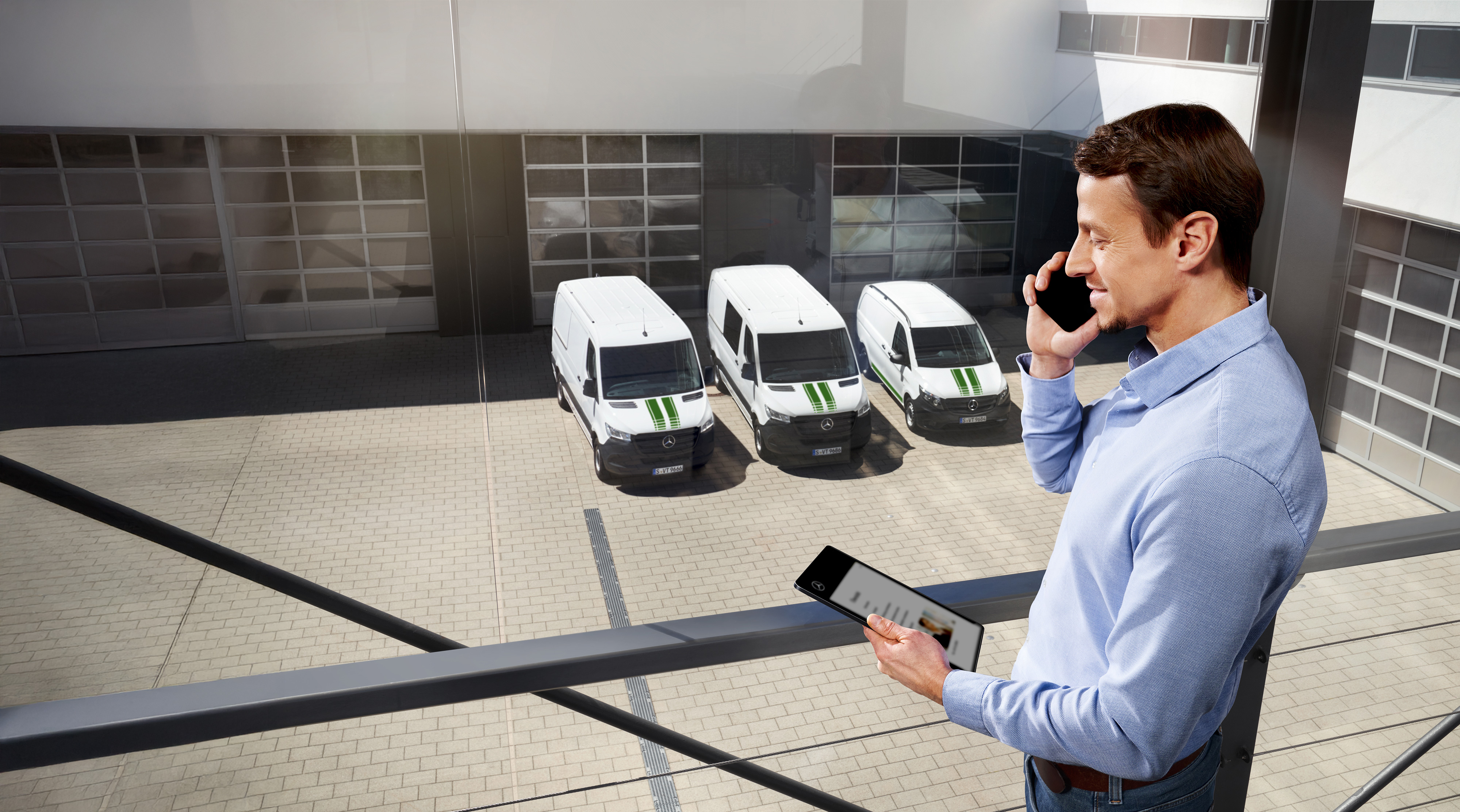 Mercedes-Benz | Transporter Qualitätsgarantie Mann am Telefon mit Tablet vor drei Mercedes-Benz Transportern, Thema: Wie lange ist die Herstellergarantie bei Mercedes-Benz?