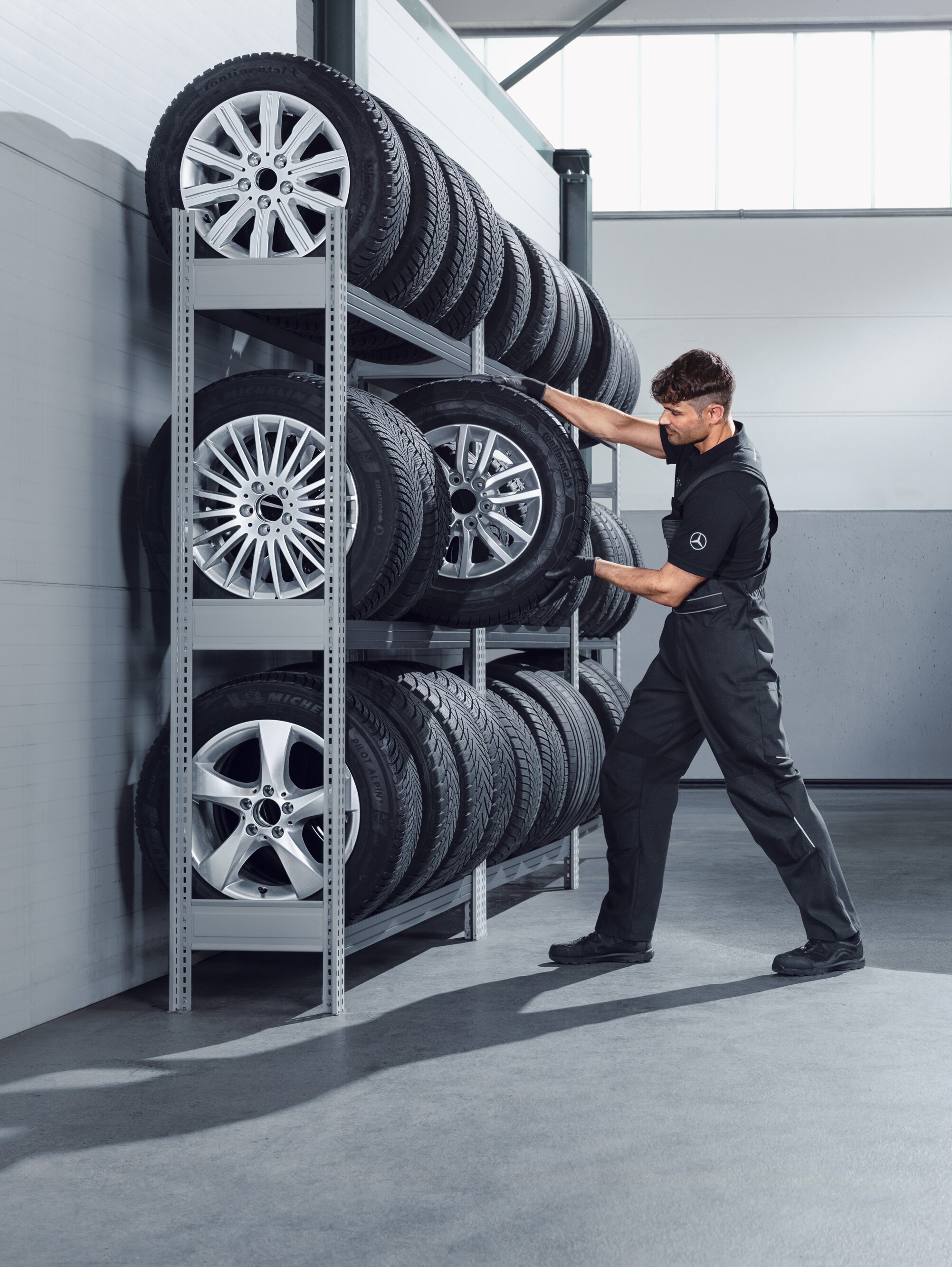 Mécanicien sélectionnant des roues hiver complètes Mercedes-Benz pour un Sprinter blanc sur les rayonnages de l'atelier.