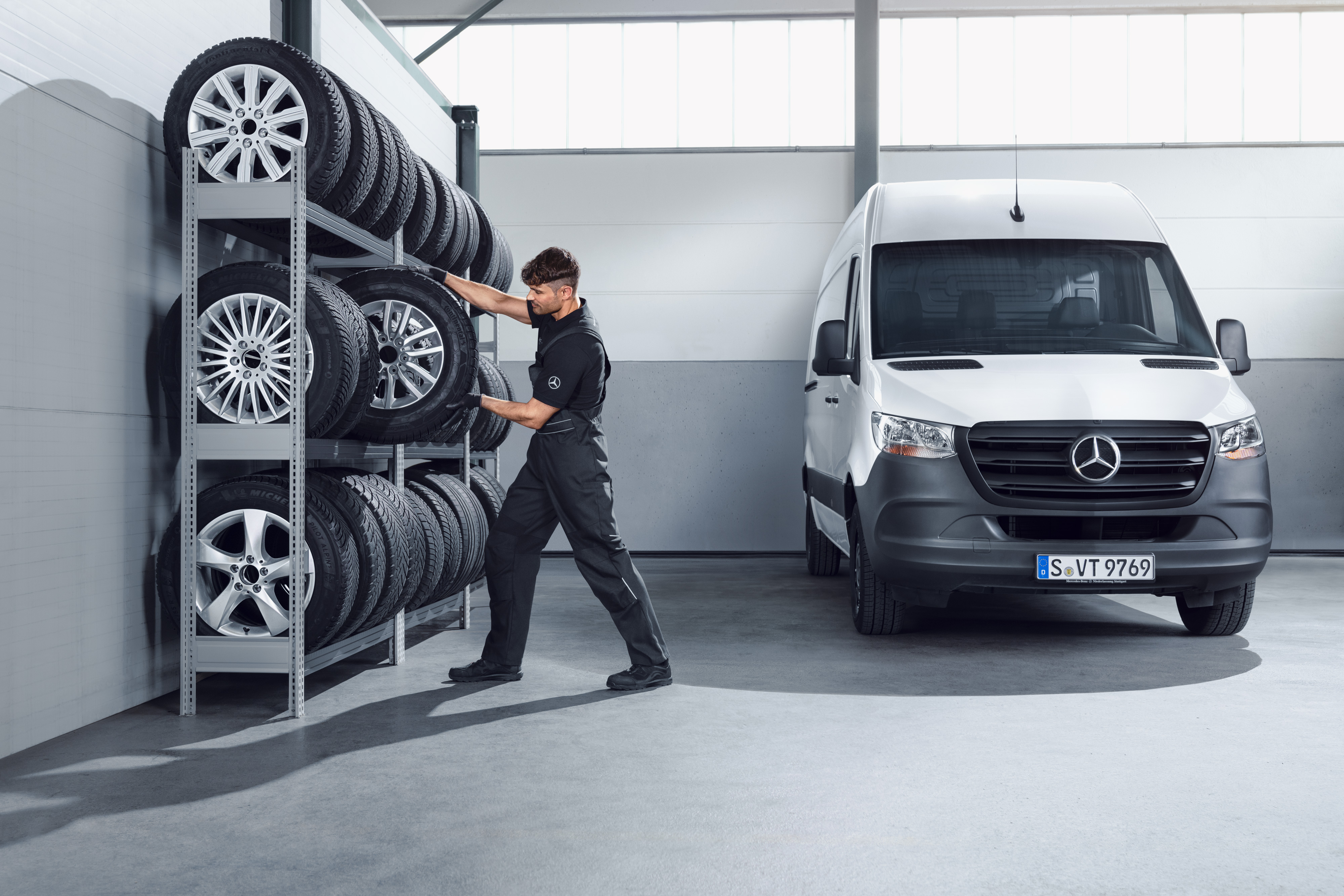 Mercedes-Benz | Pièces d'origine de qualité pour utilitaires légers Mécanicien sélectionnant des roues hiver complètes Mercedes-Benz pour un Sprinter blanc sur les rayonnages de l'atelier.