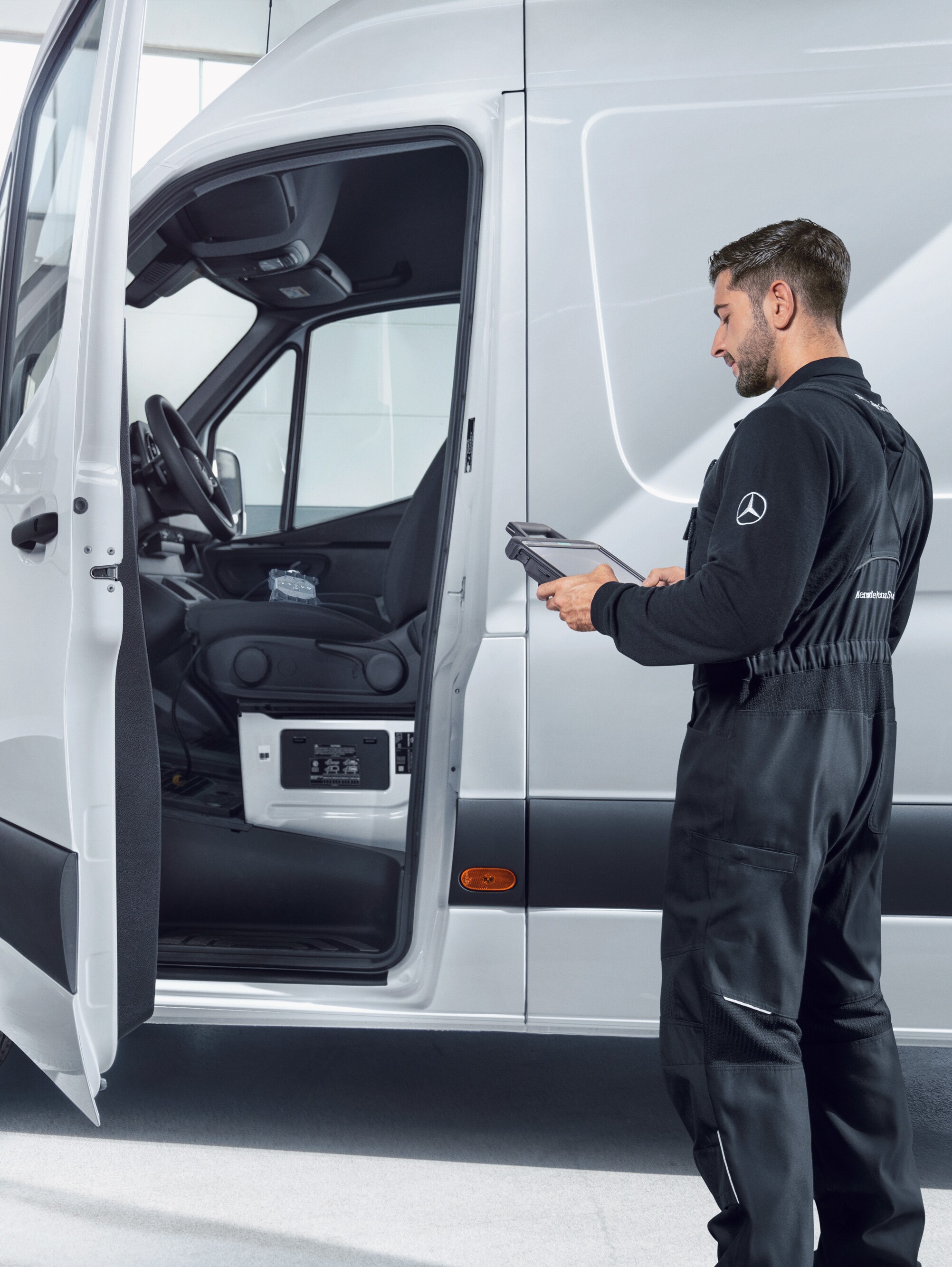 Mechaniker bei der Kontrolle eines weißen Mercedes-Benz Transporters mit einem Tablet und steht dabei für die Qualitätsstandards und das Qualitätsversprechen.