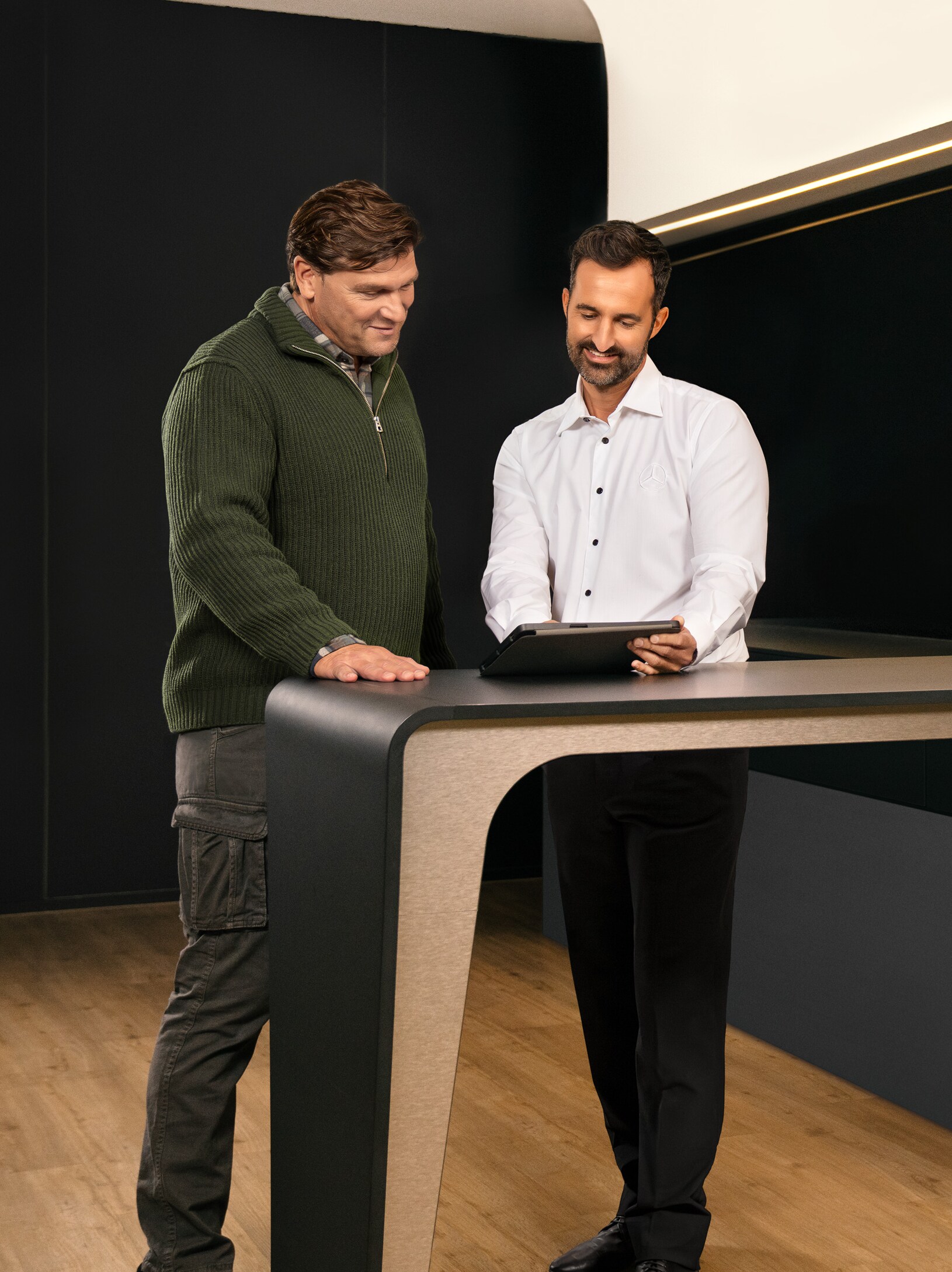 Deux hommes en consultation, debout autour d'une table, regardant un iPad.