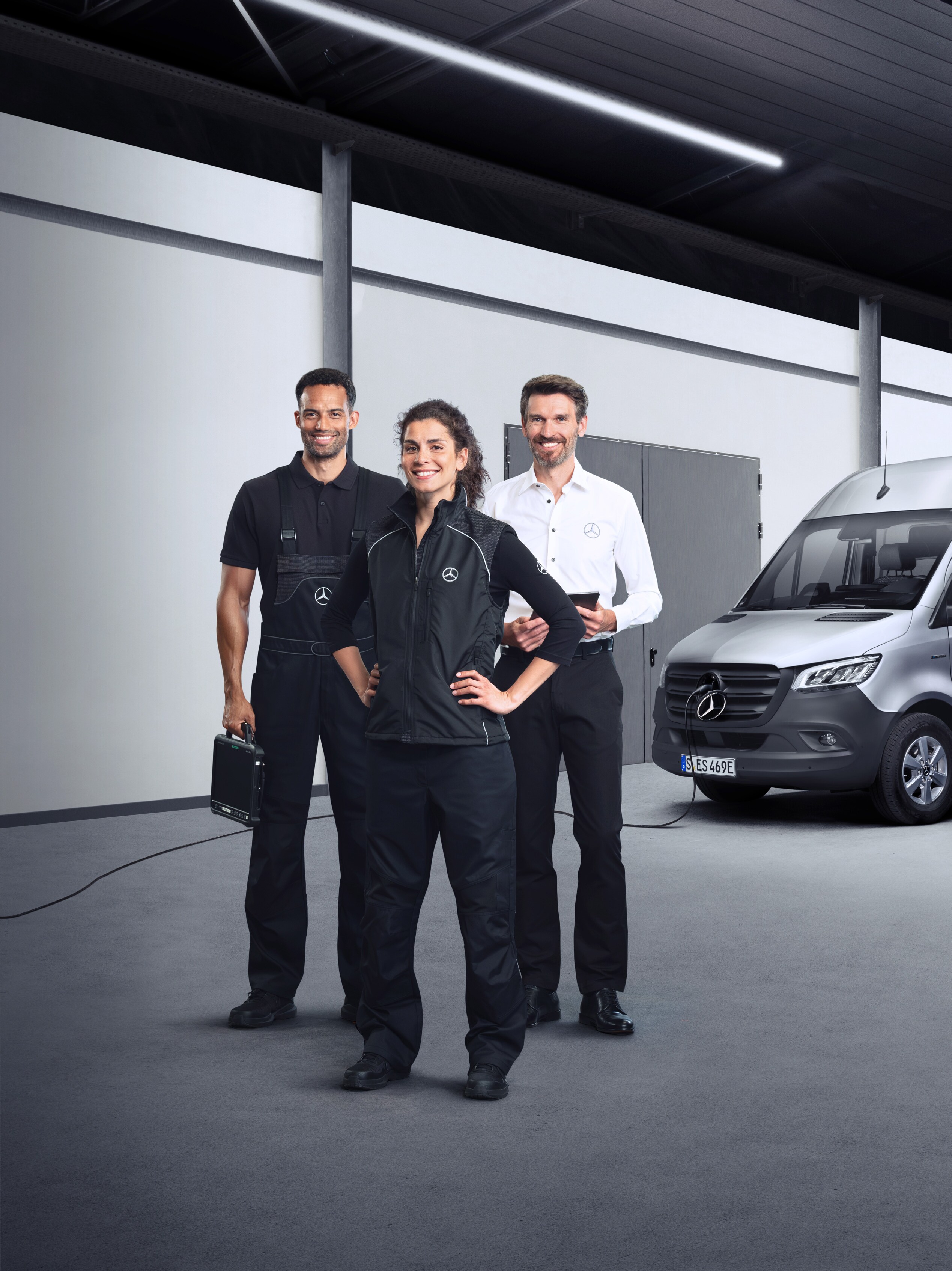 Drei Mitarbeiter stehen vor einem silbernen Mercedes-Benz eSprinter mit angeschlossenem Ladekabel.