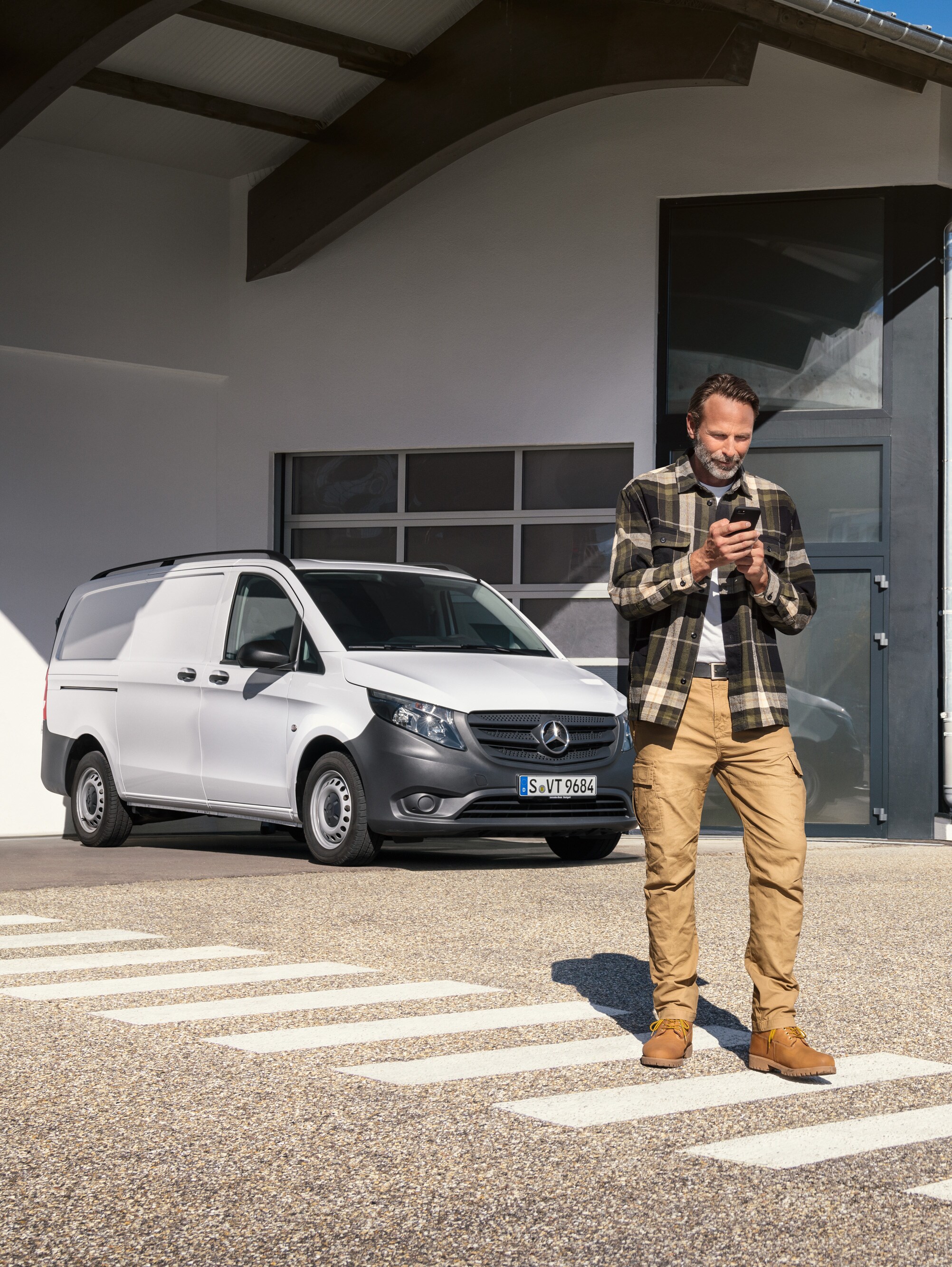 Un homme se tient devant un utilitaire léger Mercedes-Benz Vito, utilisant son smartphone.