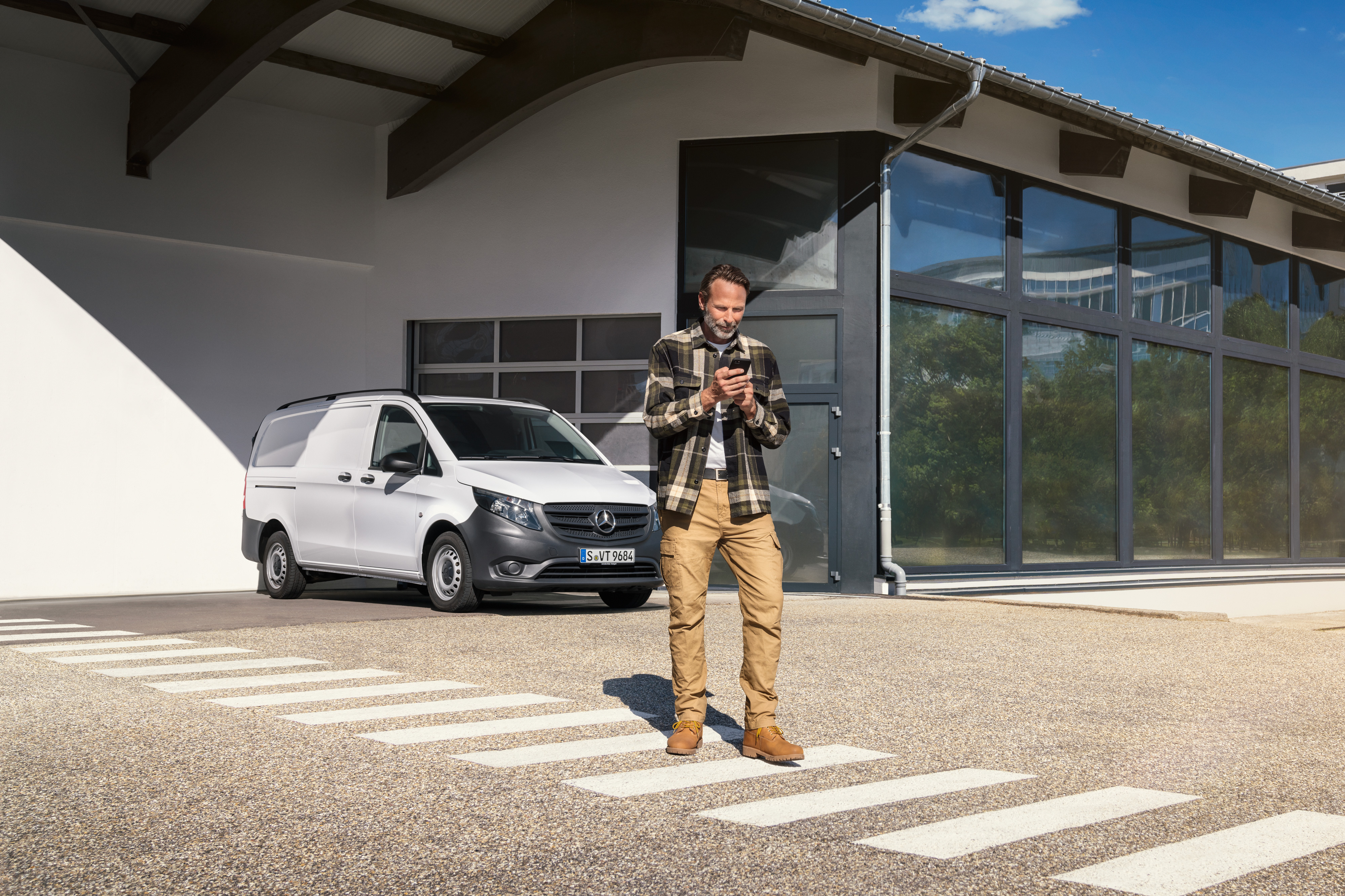 Mercedes-Benz | Services pour véhicules électriques | Support numérique Un homme se tient devant un utilitaire léger Mercedes-Benz Vito, utilisant son smartphone.