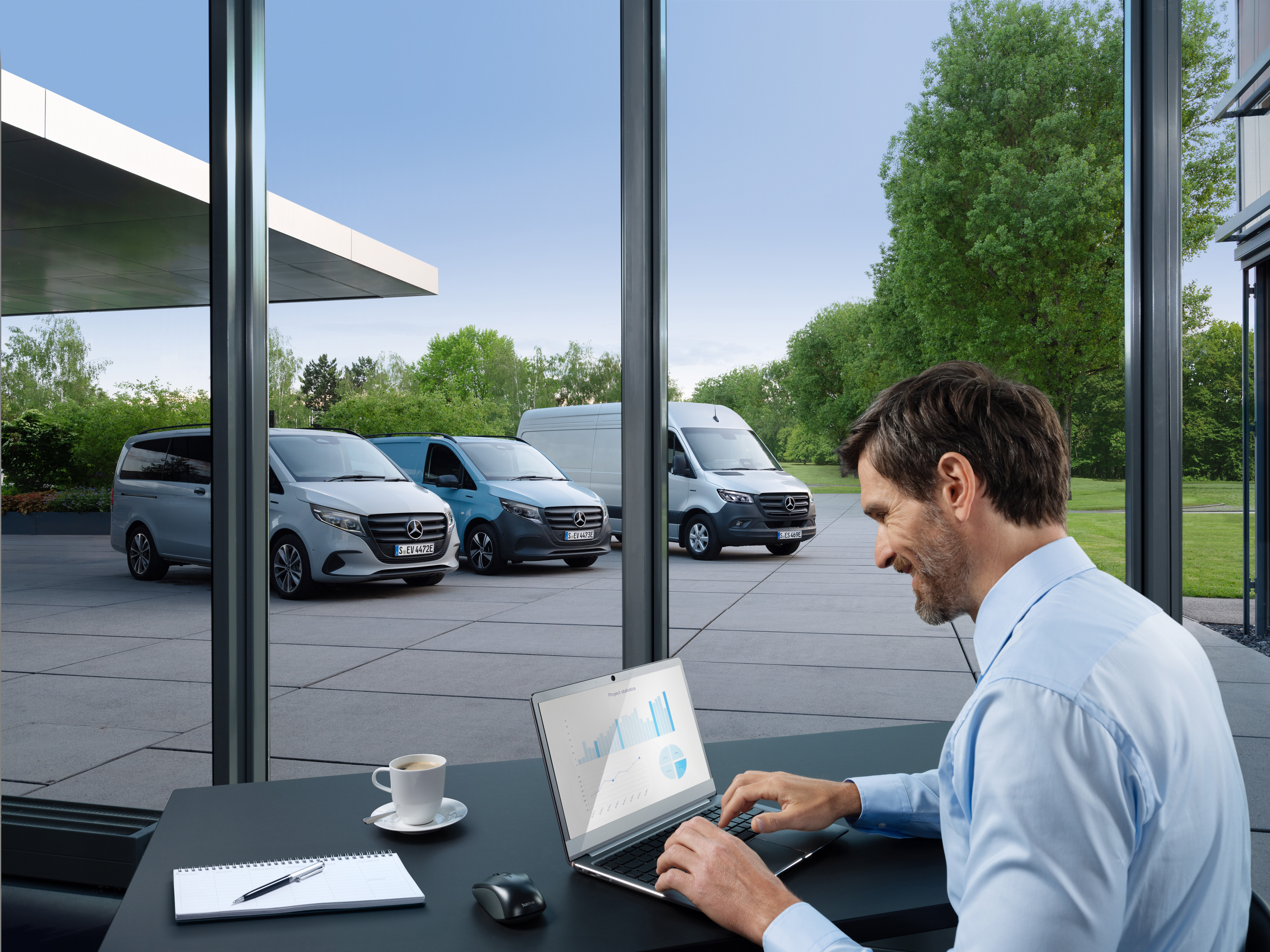 Mercedes-Benz | Services pour véhicules électriques | Packs Un homme travaille sur un ordinateur portable, à l'extérieur se trouve une série d’utilitaires légers Mercedes-Benz.
