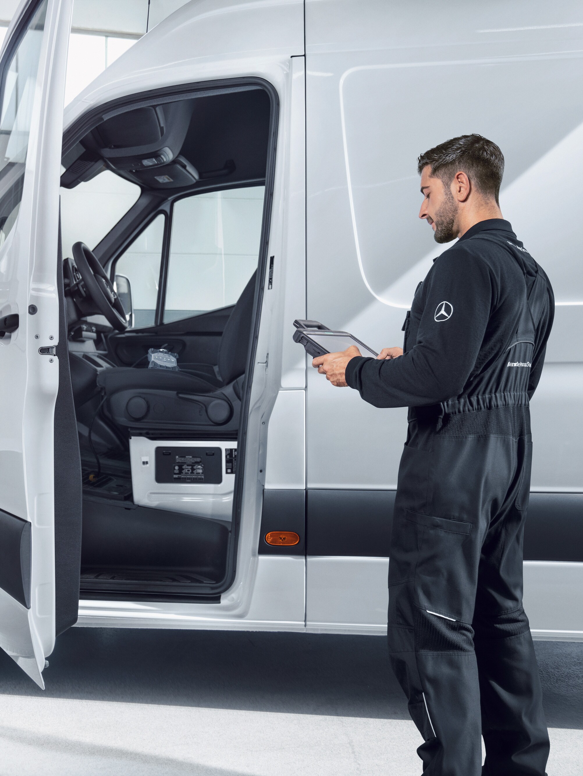 Ein Techniker überprüft einen weißen Mercedes-Benz Sprinter mit einem Tablet.