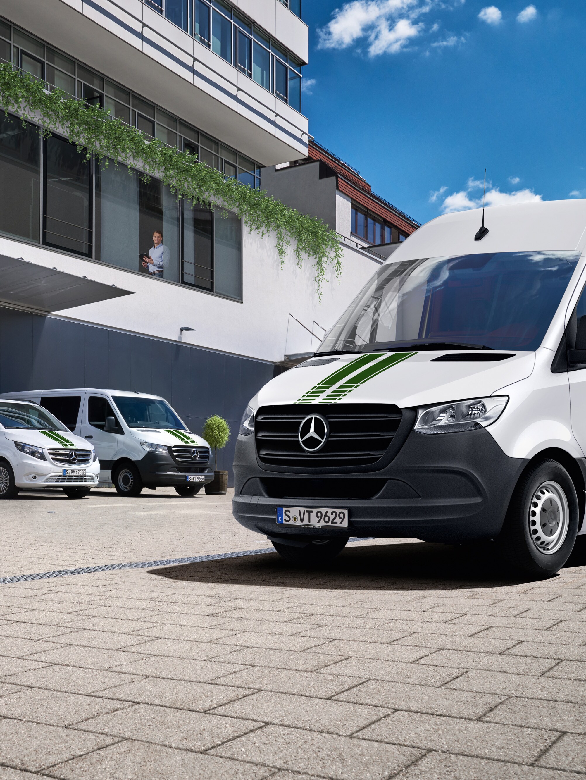 Une flotte d’utilitaires légers Mercedes-Benz blancs devant un immeuble de bureaux par une journée ensoleillée et un ciel bleu.