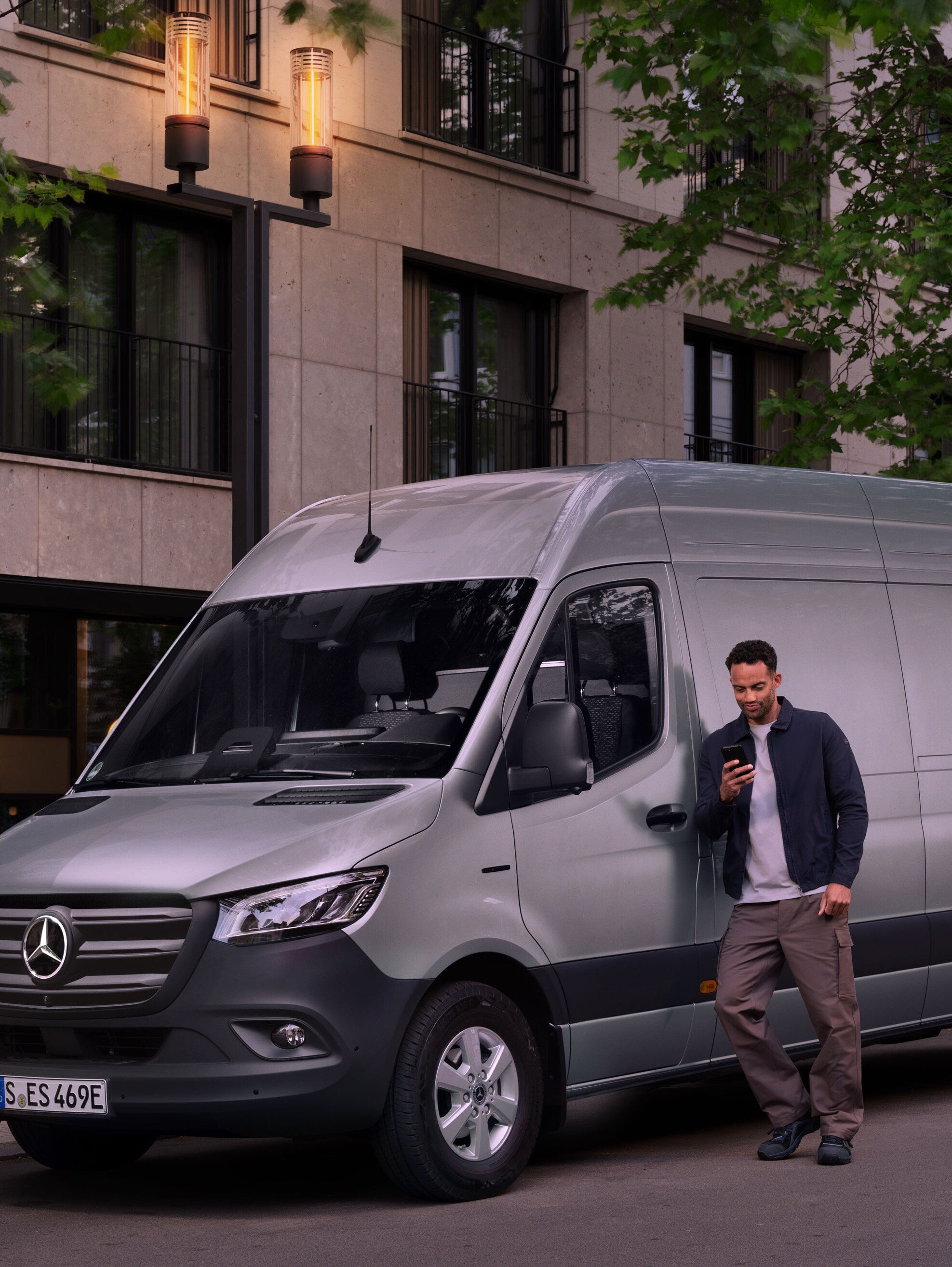 Un homme s'appuie sur un Mercedes-Benz Sprinter couleur argent et remplit une déclaration de dommage sur son téléphone portable.