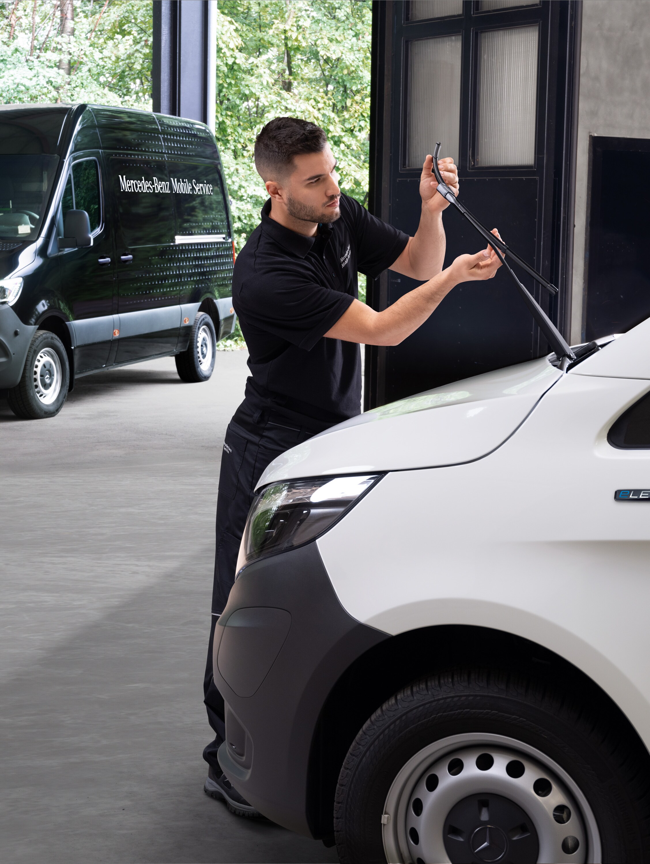 Un technicien change les balais d'essuie-glace d’un utilitaire léger Mercedes-Benz Vito blanc.