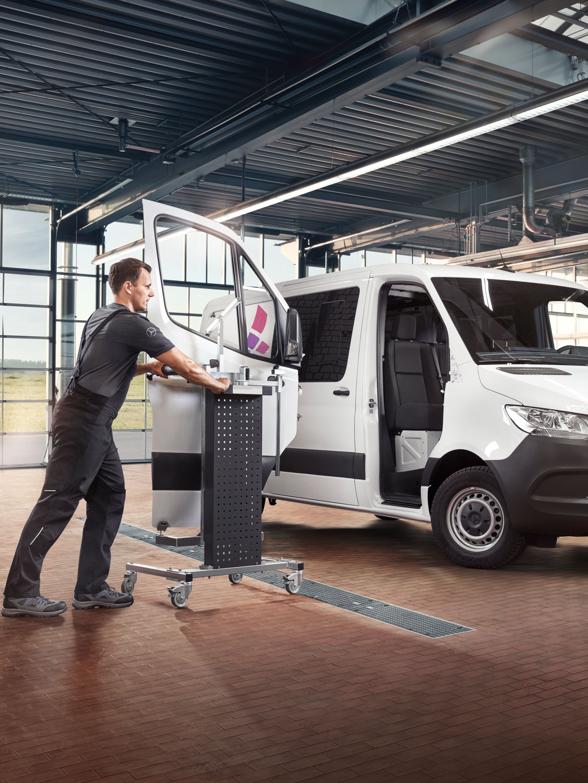Un mécanicien fixe la porte d’une Mercedes-Benz Sprinter blanche.