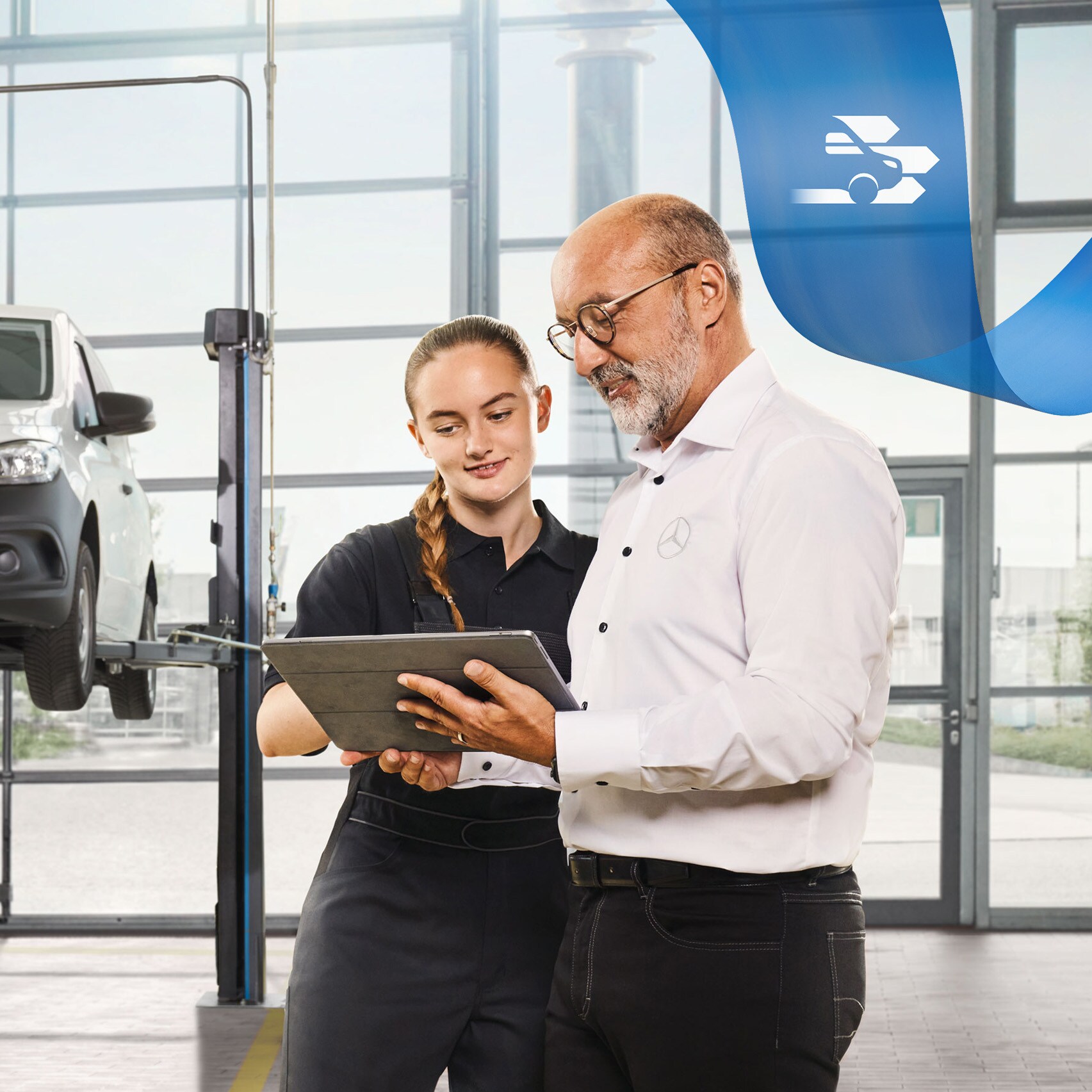 Deux employés discutent de l'entretien d'un véhicule industriel à côté d'un utilitaire léger Mercedes-Benz sur cric dans l'atelier.