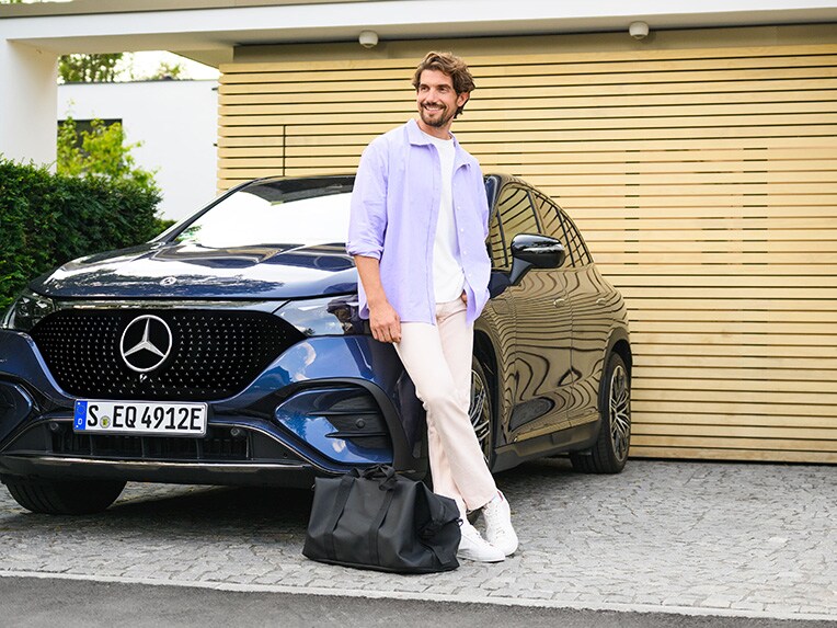 Une personne s'appuyant contre un véhicule Mercedes-Benz devant sa maison.
