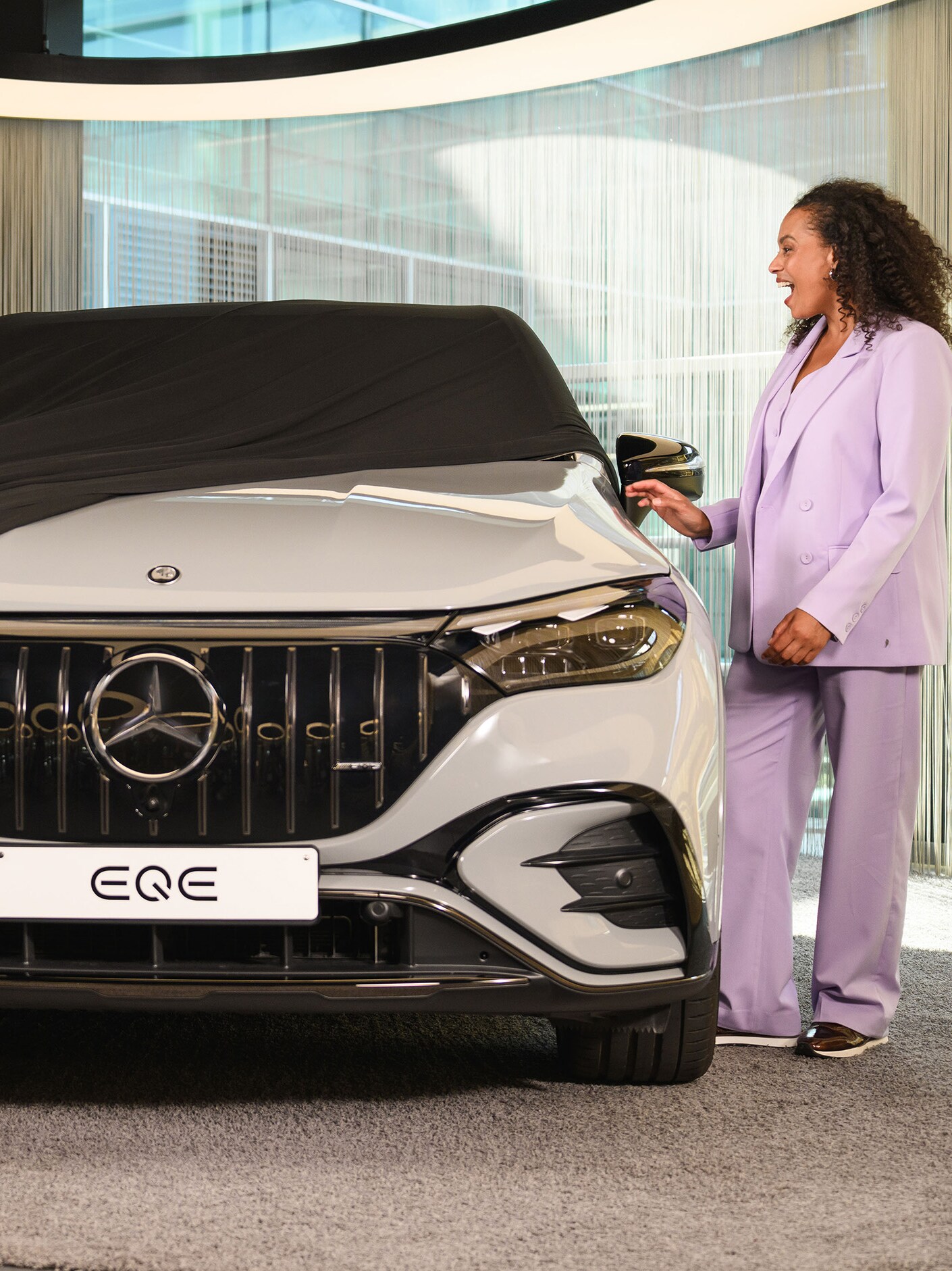 Zwei Personen und ein Kind ziehen eine Abdeckung von einem neuen Mercedes-Benz Fahrzeug in einem Showroom ab.