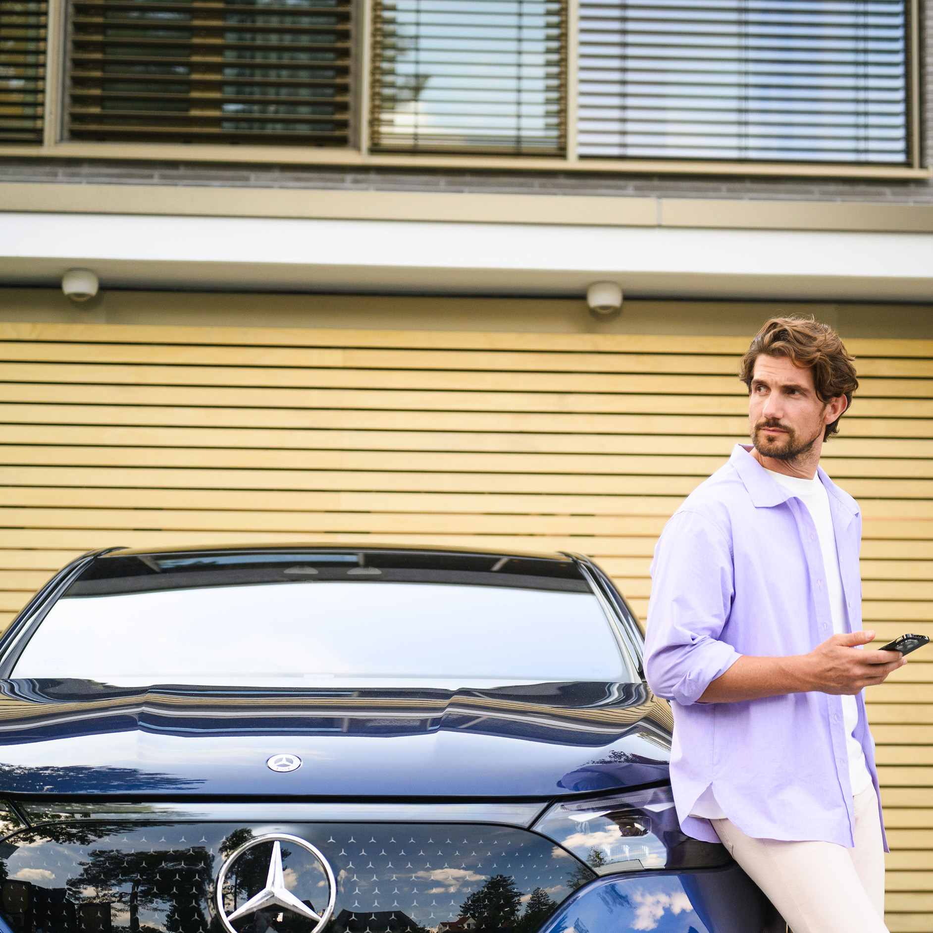 Offre de financement pour votre Mercedes-Benz d’occasion Une personne appuyée contre un véhicule Mercedes-Benz, regardant au loin et tenant un appareil mobile.