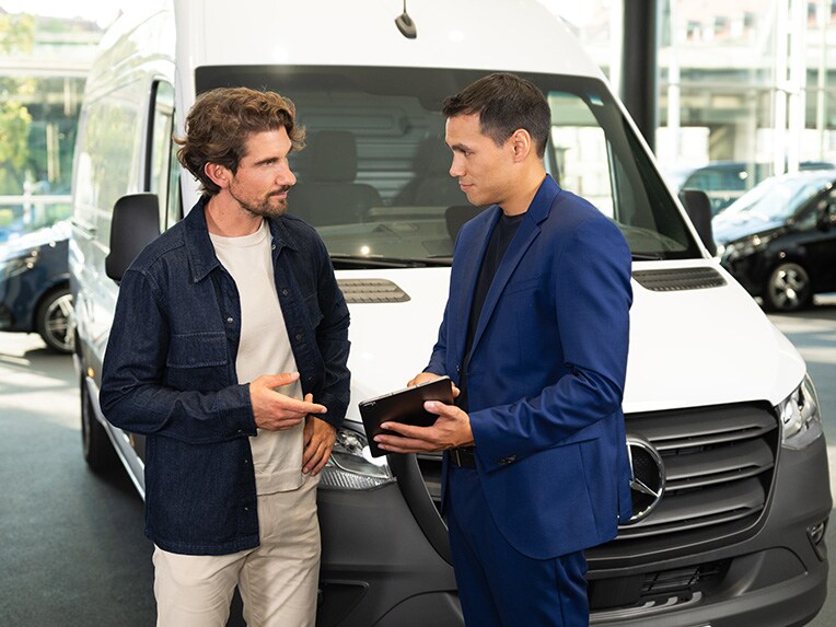 Zwei Personen diskutieren und zeigen op ein mobiles Gerät, während sie vor einem Mercedes-Benz Nutzfahrzeug stehen.