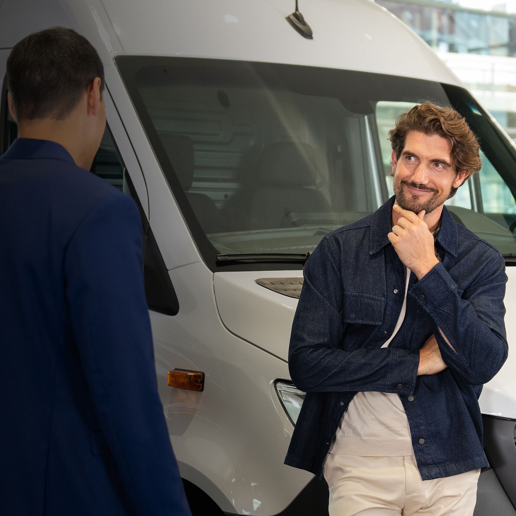 Kunde im Gespräch mit einem Berater neben einem weißen Mercedes-Benz Transporter im Showroom.